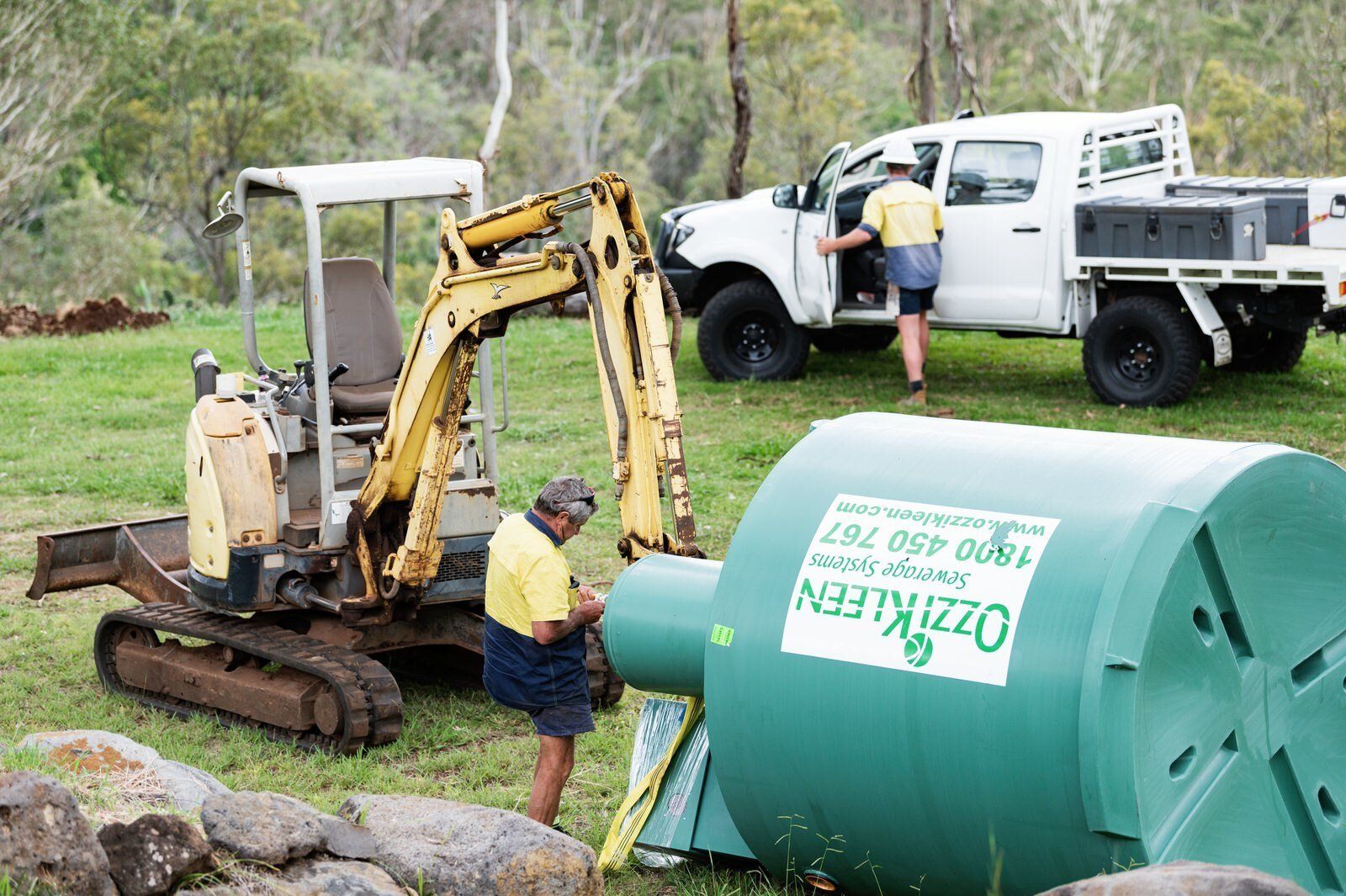 A HC Plumbing ute parked behind an excavator about to lift a new OzziKleen House Sewerage Treatment Plant into position in Toowoomba