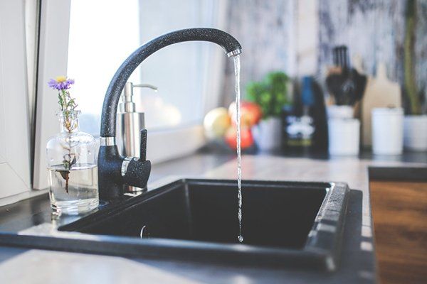 A picture of a black kitchen tap running into a black sink