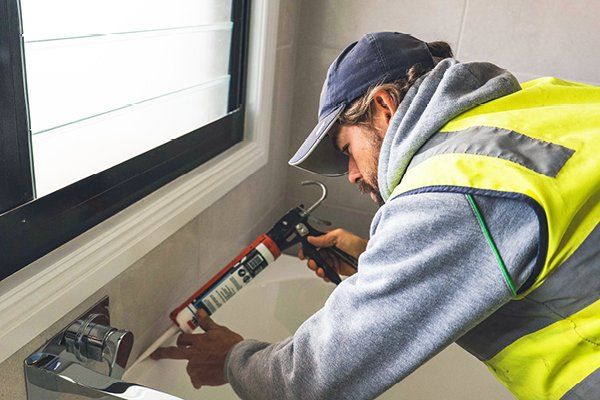 A picture of one of our plumbers caulking around a new bath tub