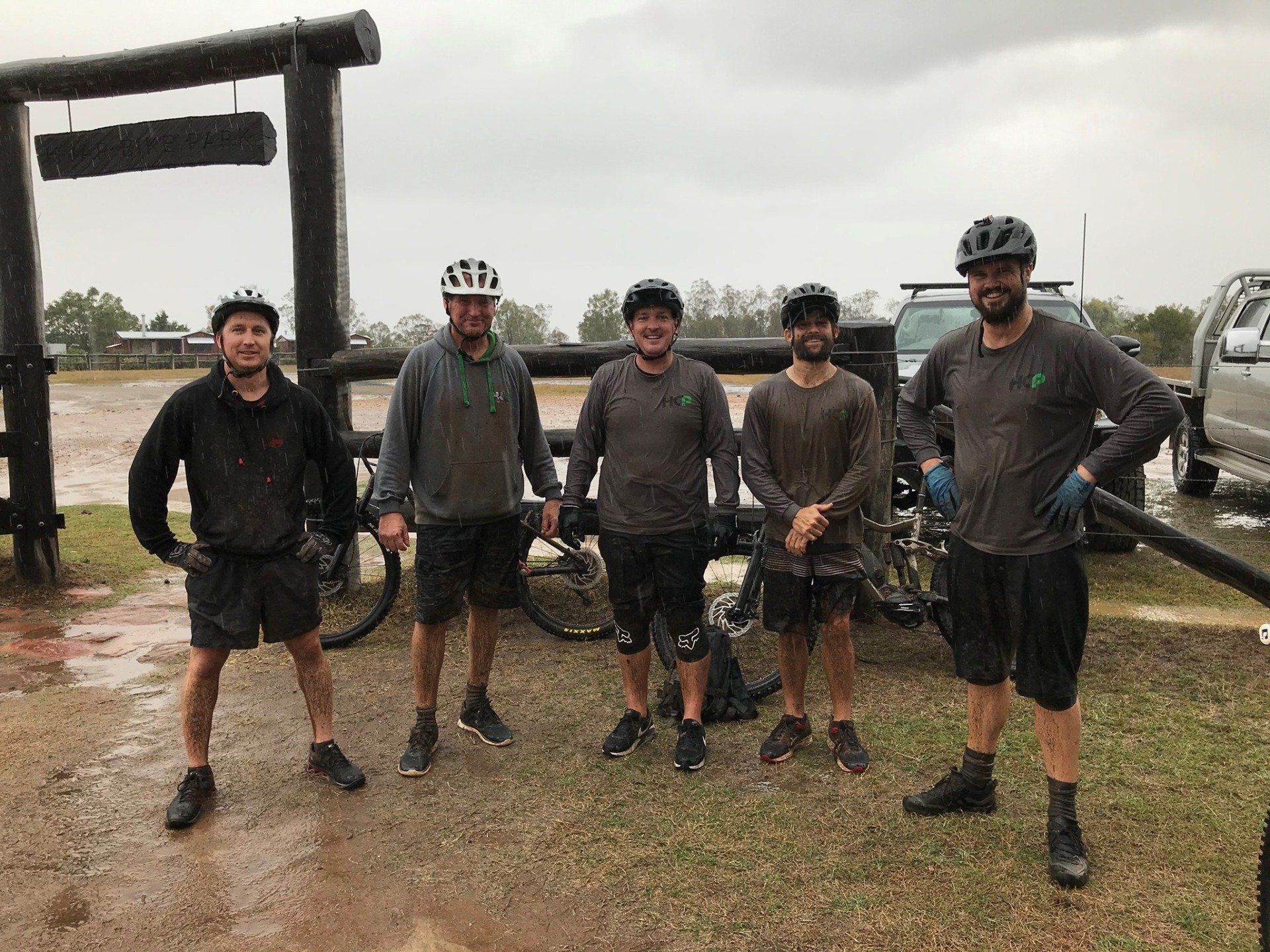 5 men in HCP branded shirts and helmets, standing in front of bikes in the pouring rain with huge smiles on their faces.