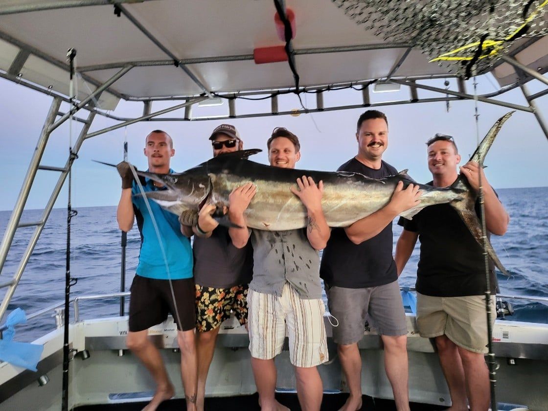 A picture of 5 of our team members holding an enormous marlin on the back of a charter boat