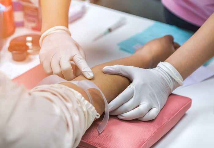 Nurse preparing injection to patient's arm for blood drawing.