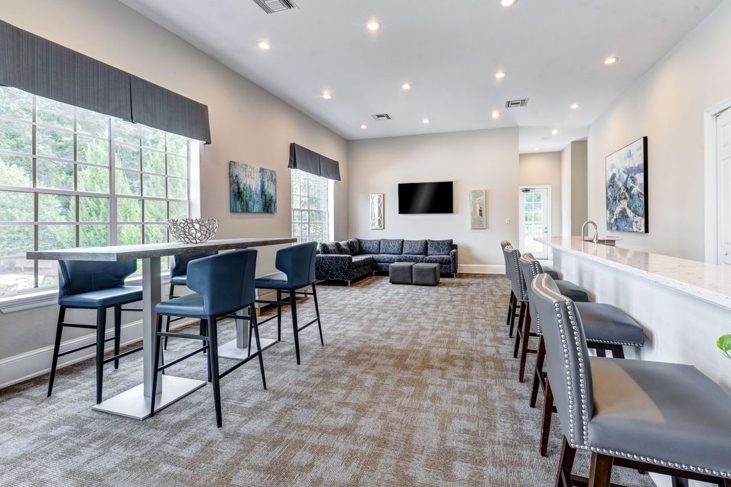 A lounge area with a bar, high-top table, and seating, in a bright room with windows and a TV.