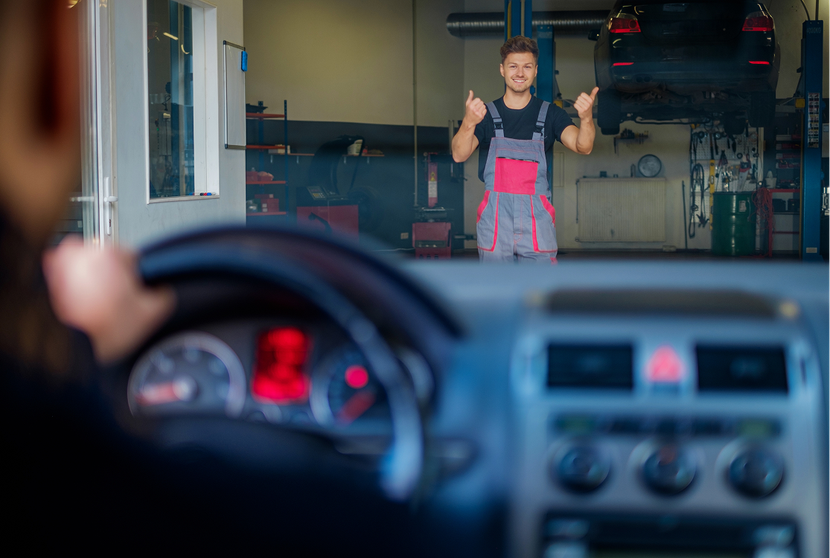 Mechanic giving thumbs up, visible from inside a car in a garage. | Lambert's Auto Repair