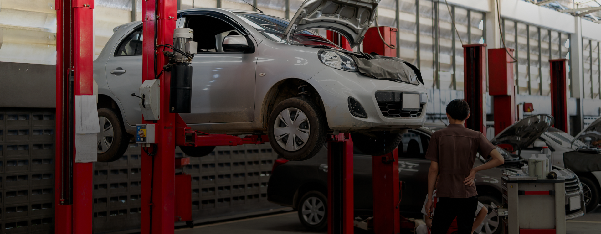 Car on a lift in a mechanic's shop. A person stands near another car. | Lambert's Auto Repair