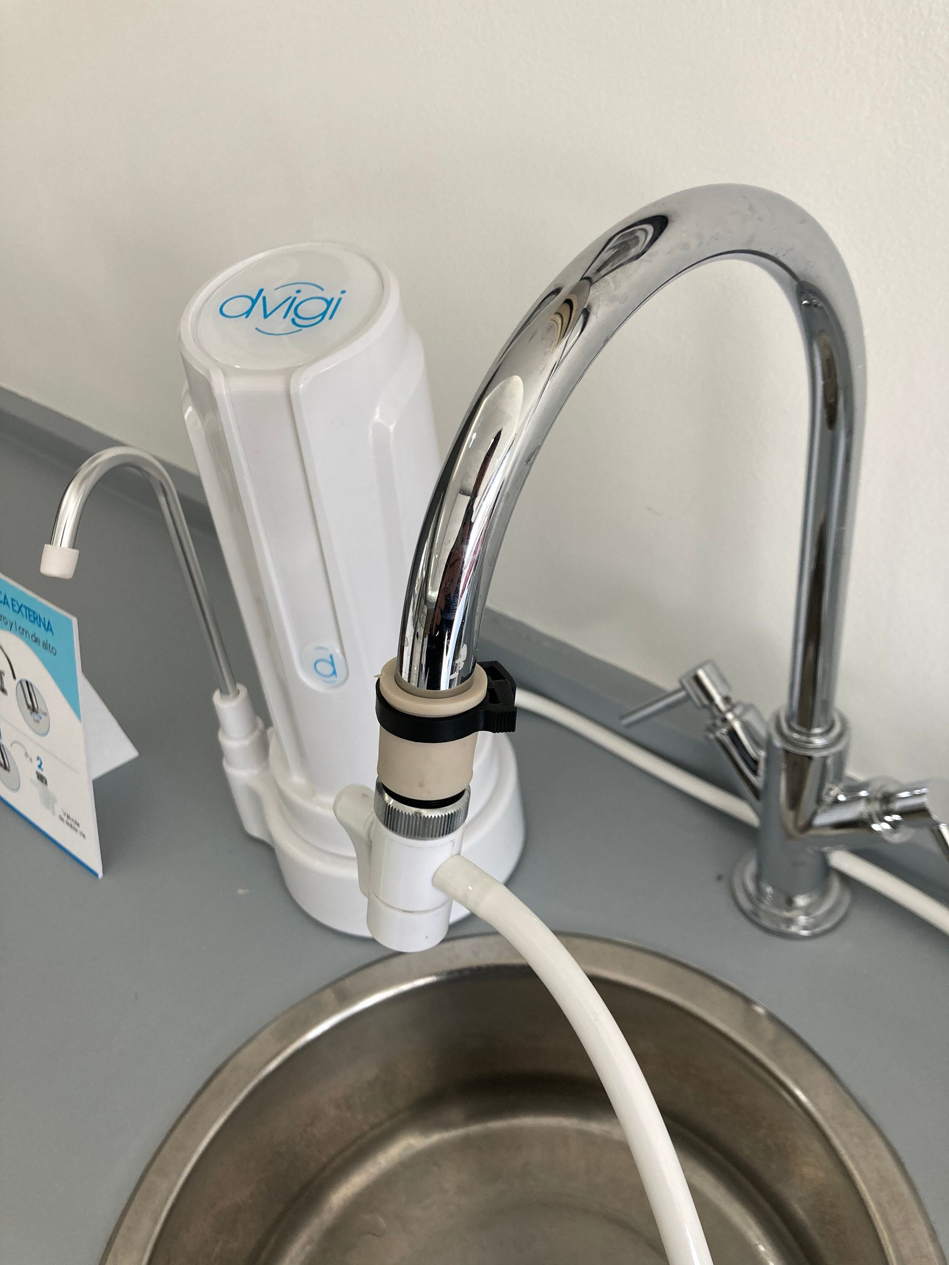 Filtro de agua blanca conectado a un grifo cromado sobre un fregadero de acero inoxidable.
