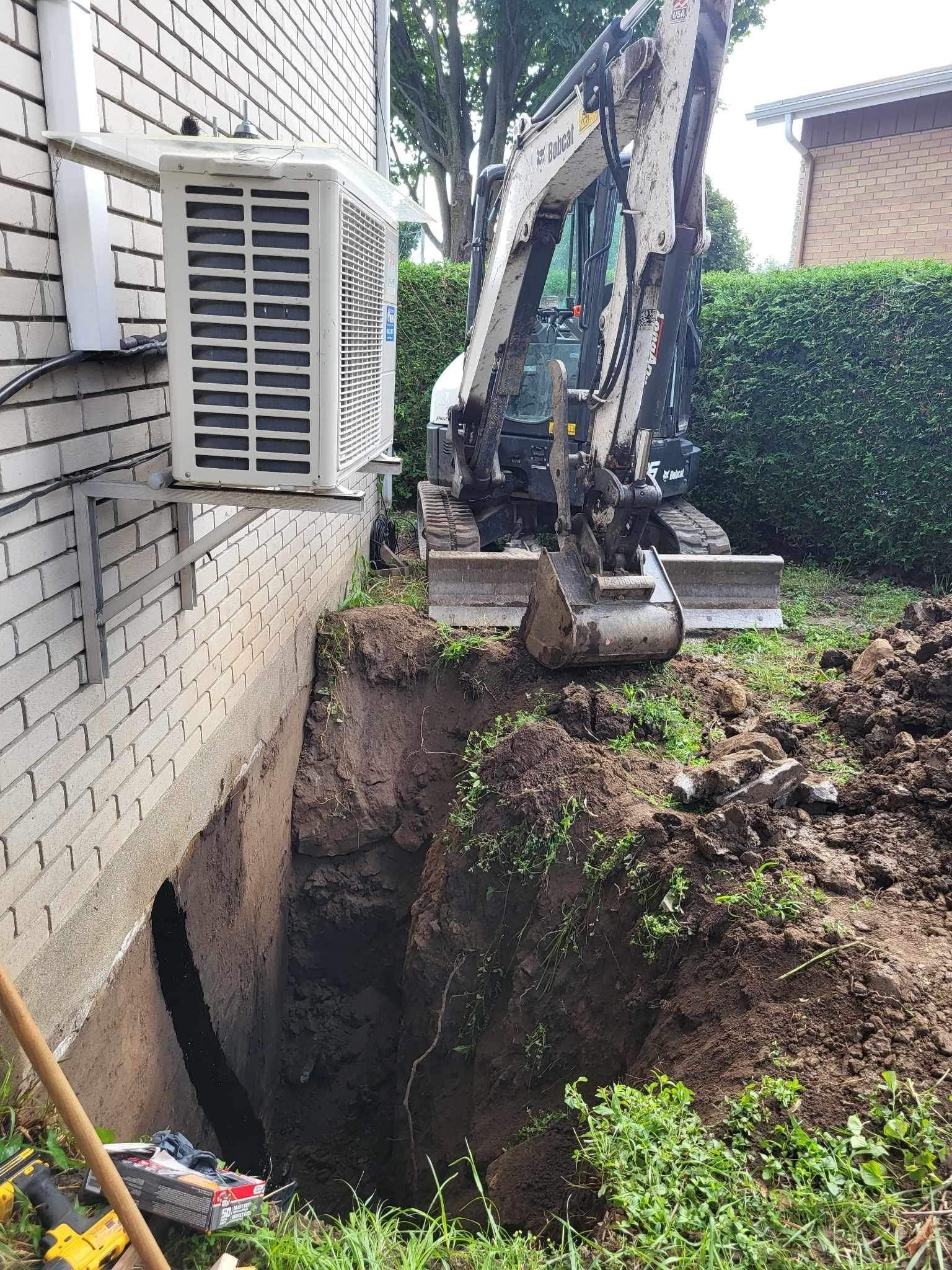 An excavator is digging a hole in the ground next to a house.