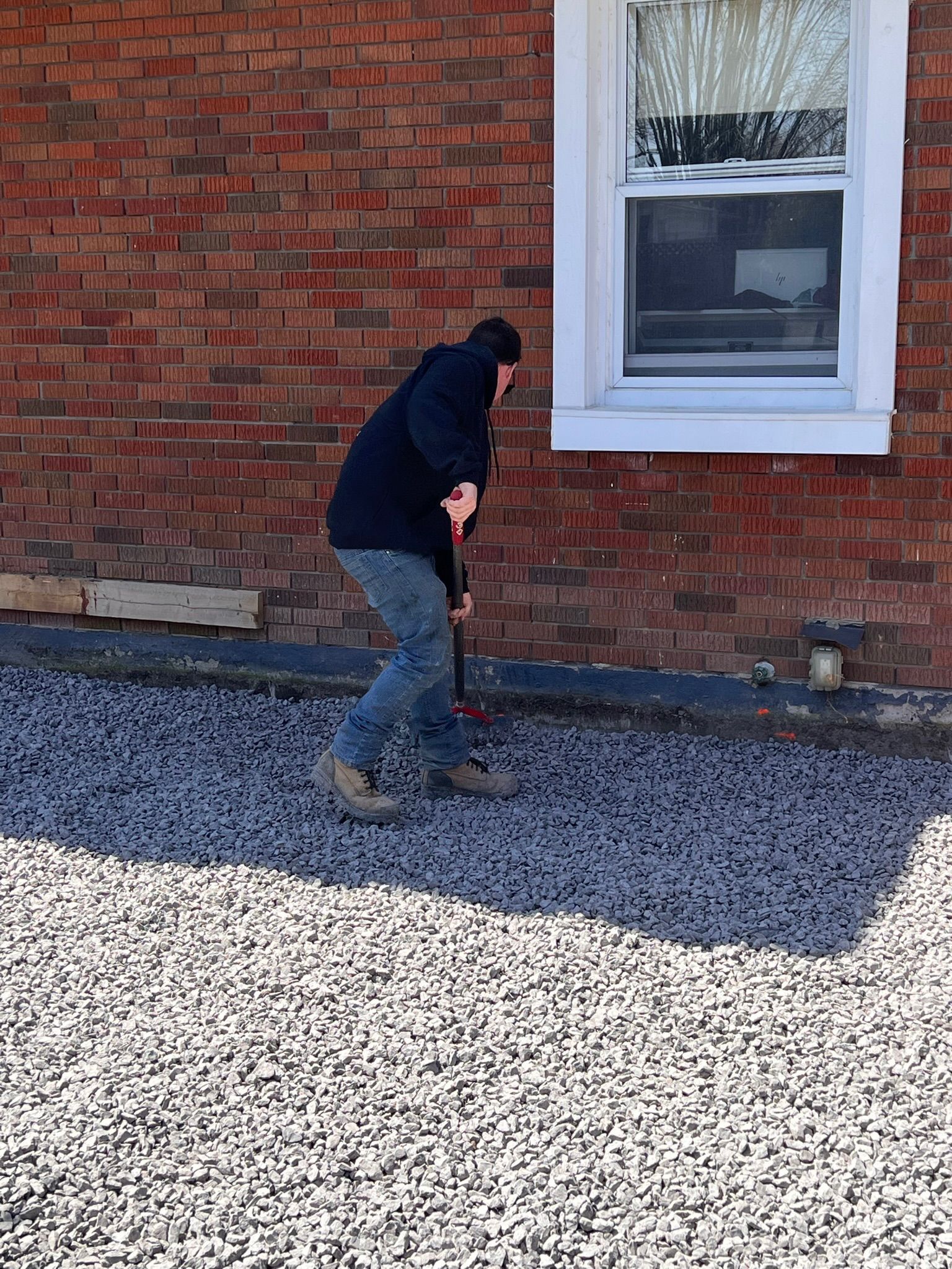 Un homme se tient devant un bâtiment en brique et tient une pelle.