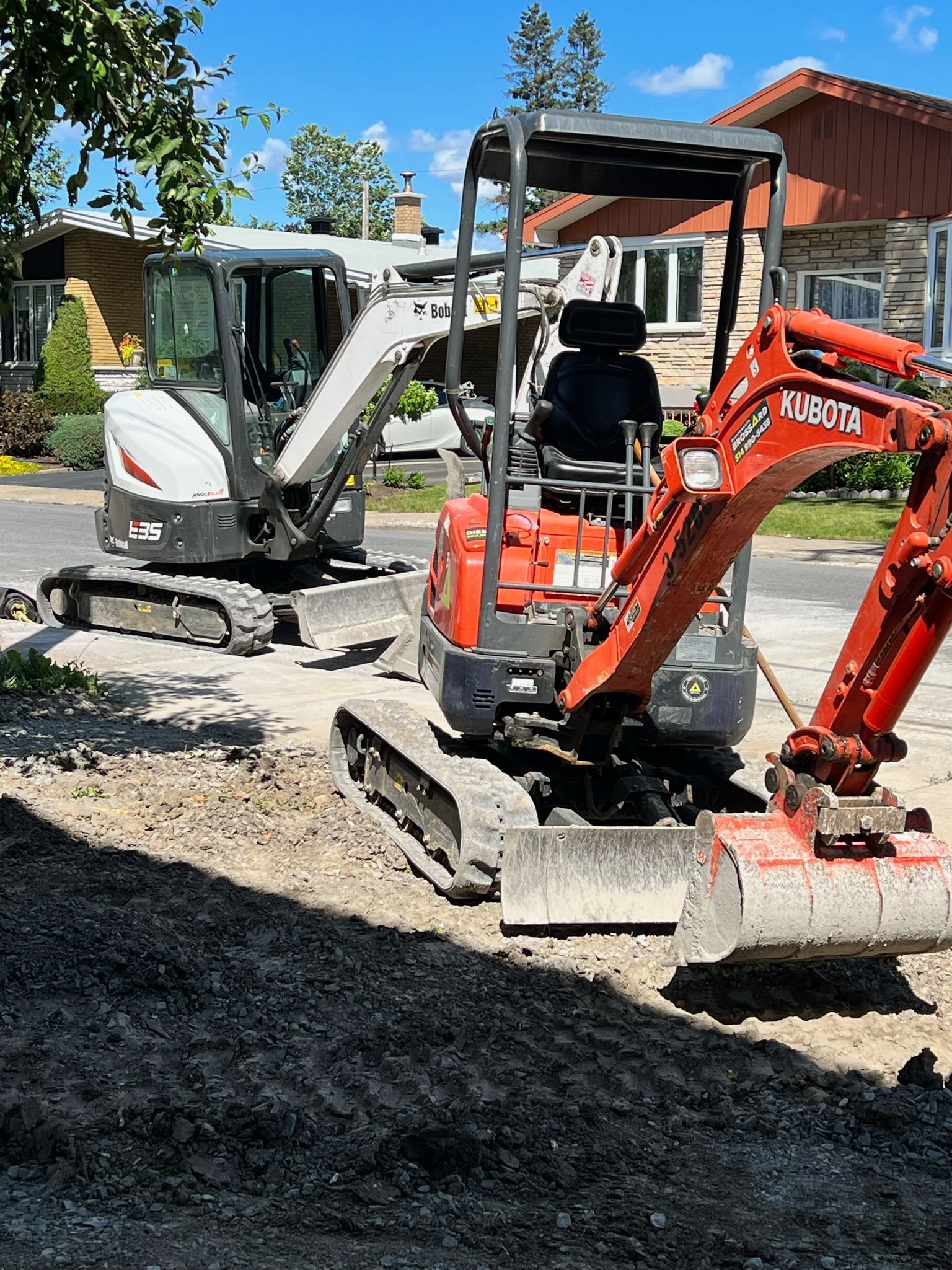 Deux excavatrices travaillent sur un chantier de construction devant une maison.