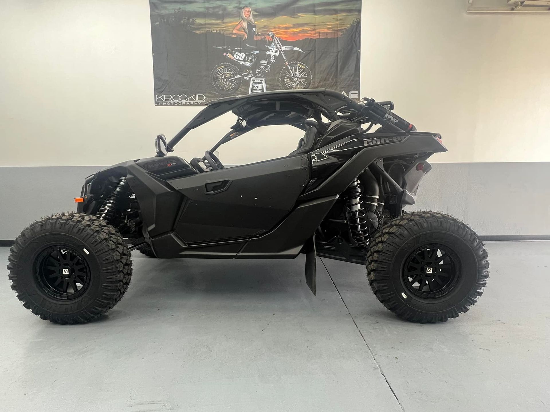 A black atv is parked in a garage in front of a wall with a picture of a motorcycle on it.