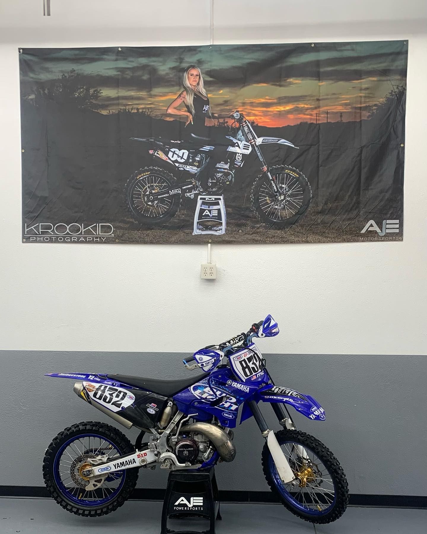 A blue dirt bike is parked in front of a poster on the wall.