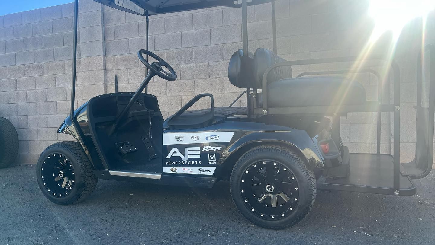 A black golf cart is parked in front of a brick wall.