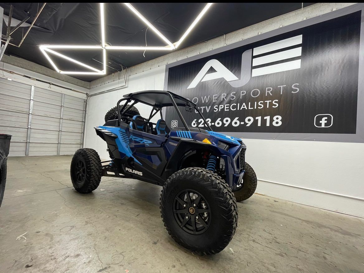 A blue atv is parked in a garage next to a sign that says ae sports atv specialists.