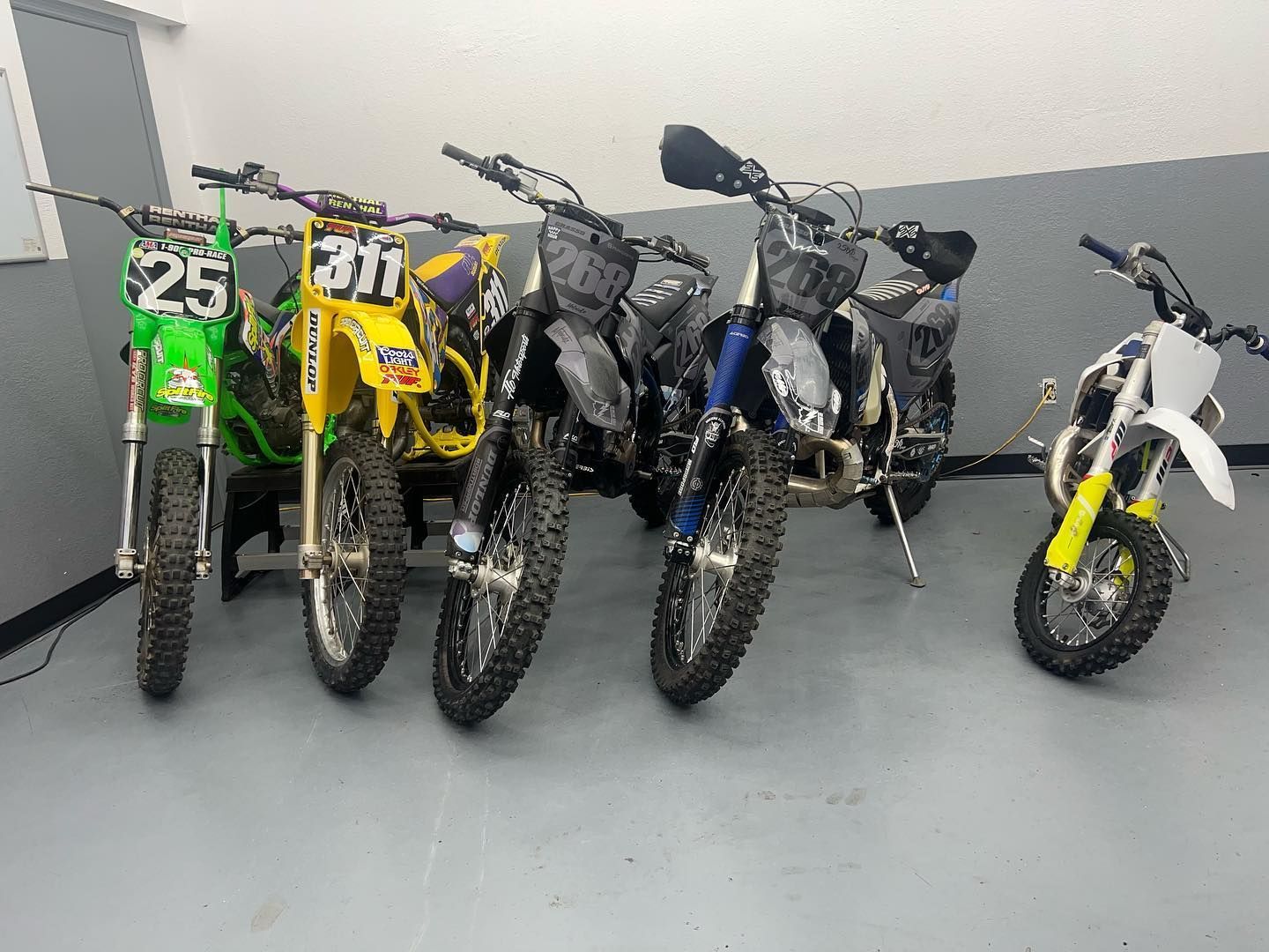 A group of dirt bikes are parked next to each other in a garage.