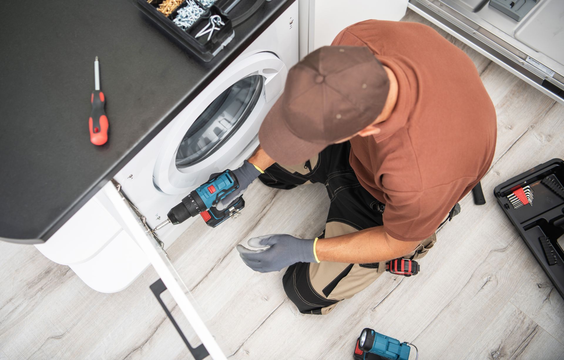 A man is kneeling on the floor fixing a washing machine.