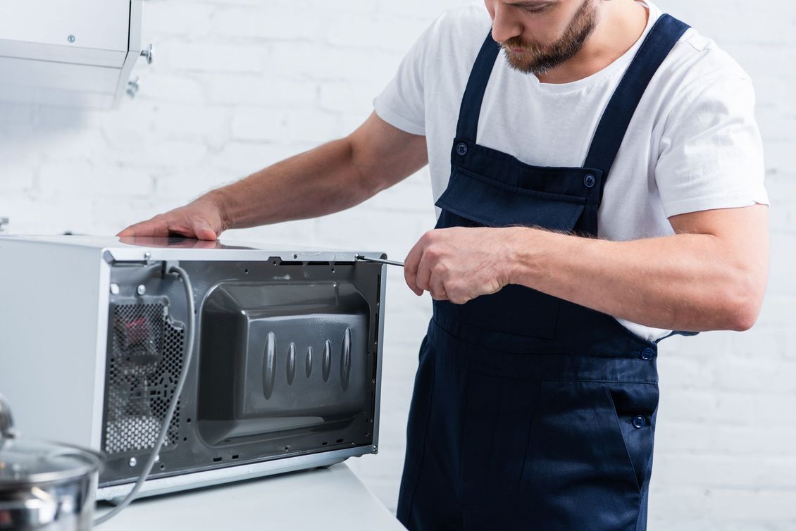 A man is fixing a microwave oven in a kitchen.