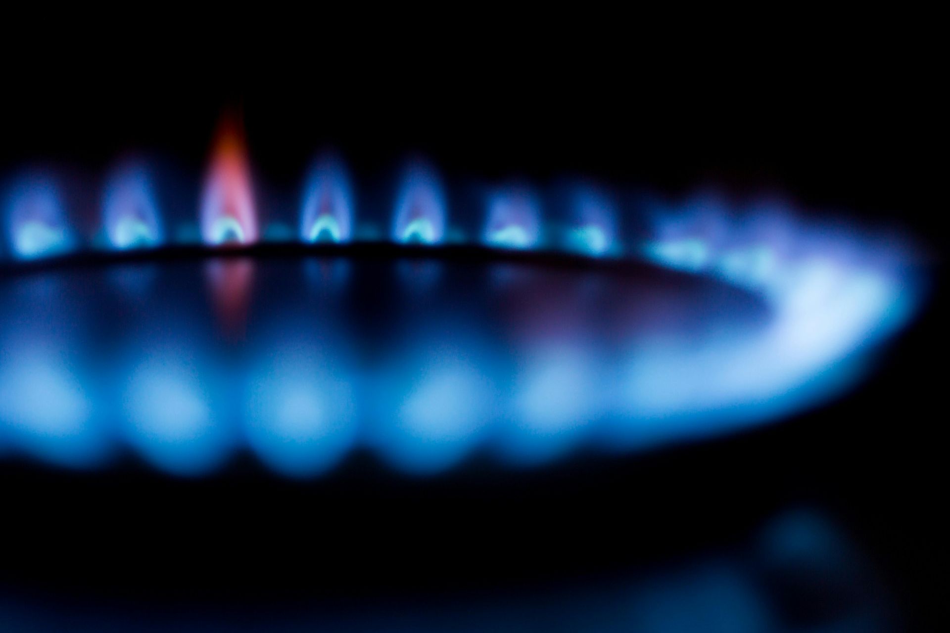 A close up of a gas burner with blue flames on a black background.