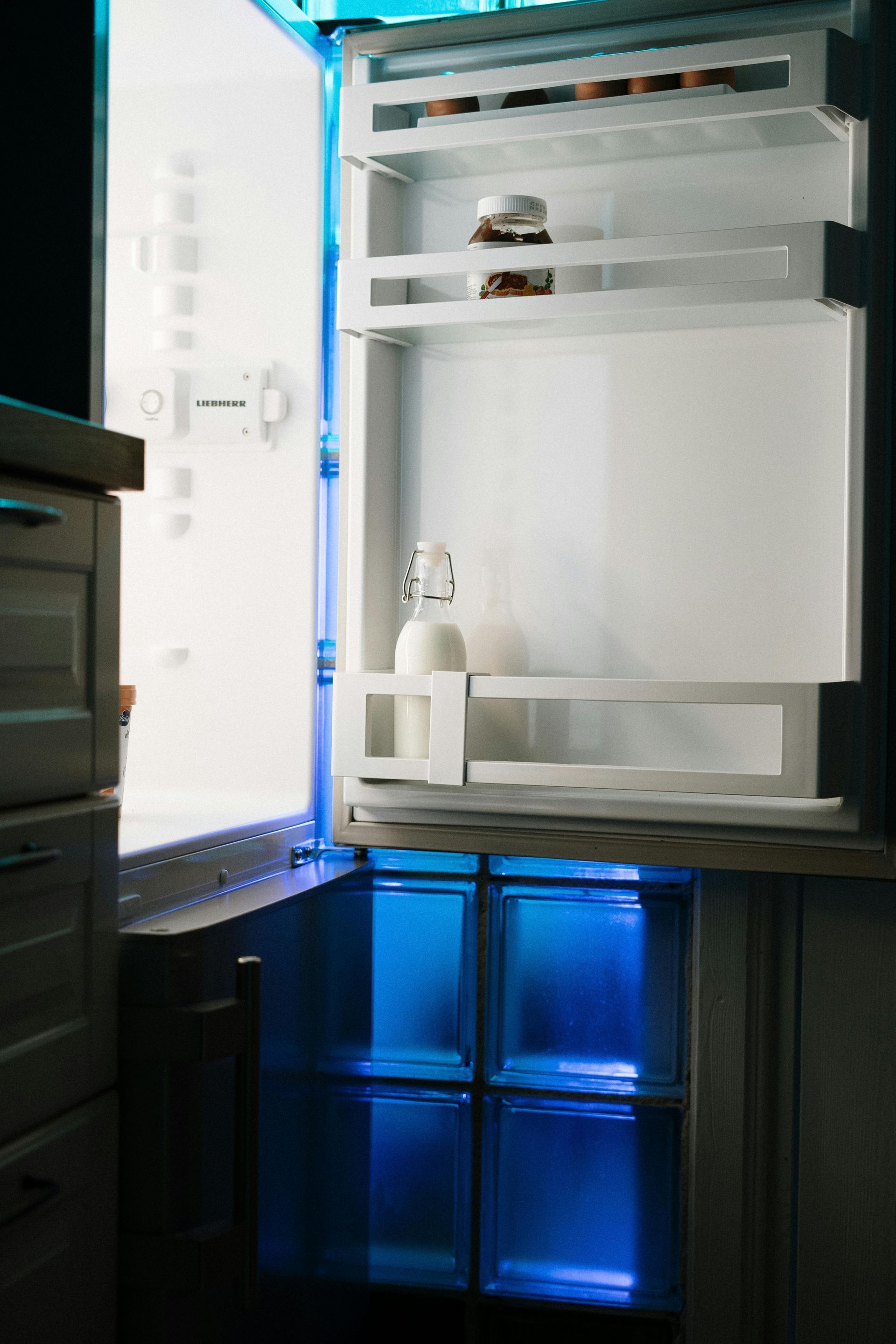 A refrigerator with the door open and a bottle of milk on the shelf.