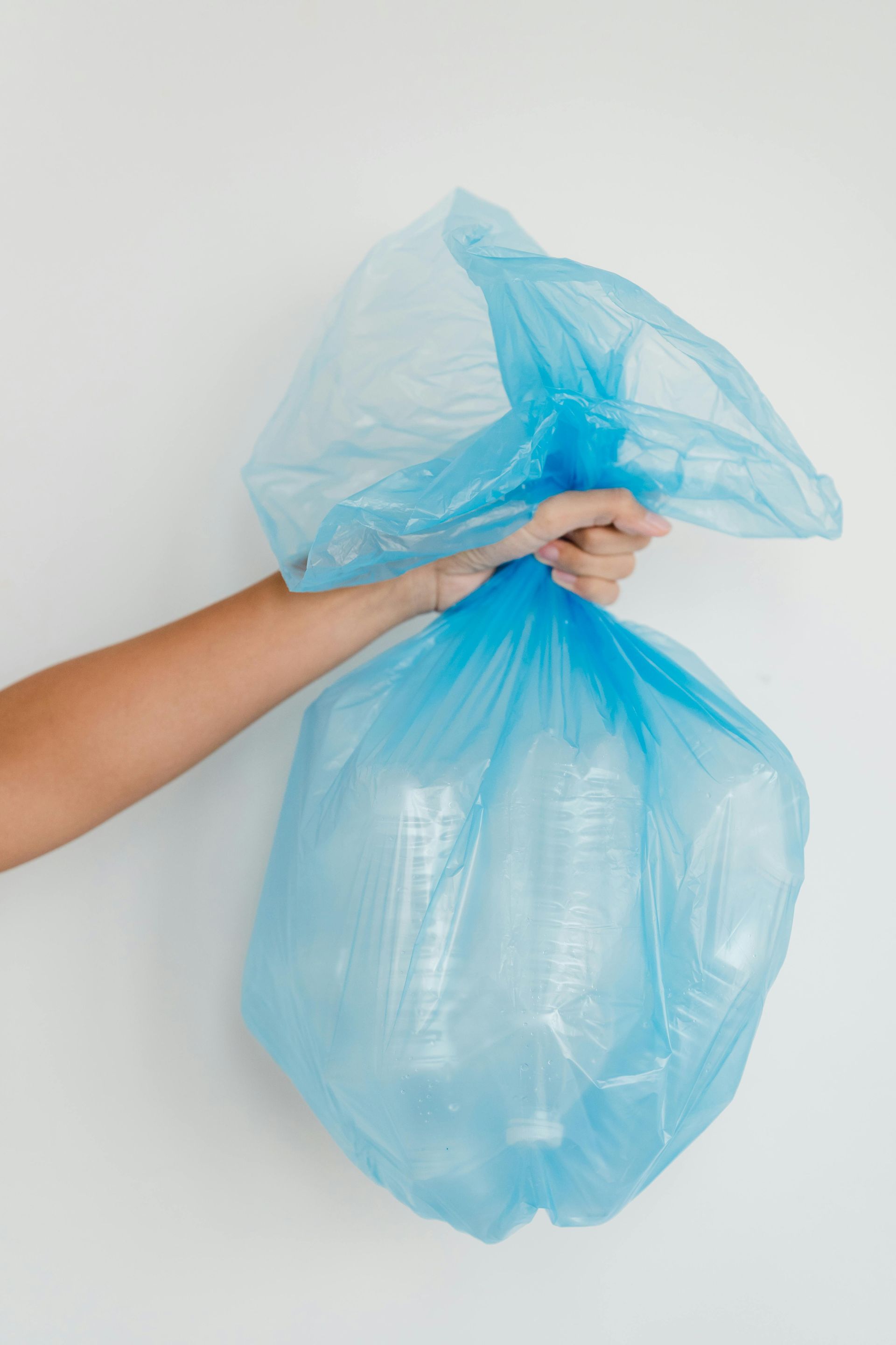 A person is holding a blue plastic bag filled with plastic bottles.