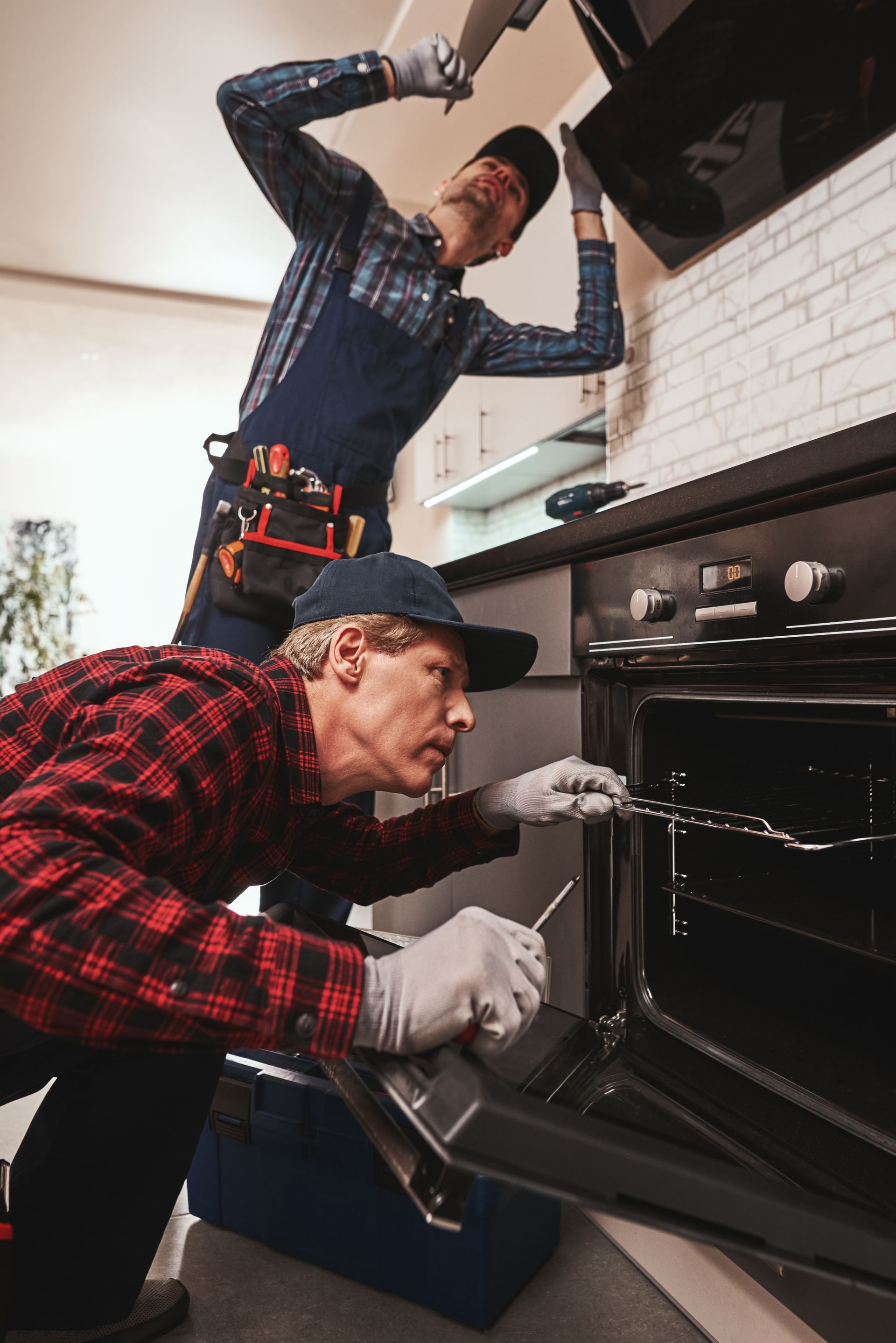 Two men are working on an oven in a kitchen.