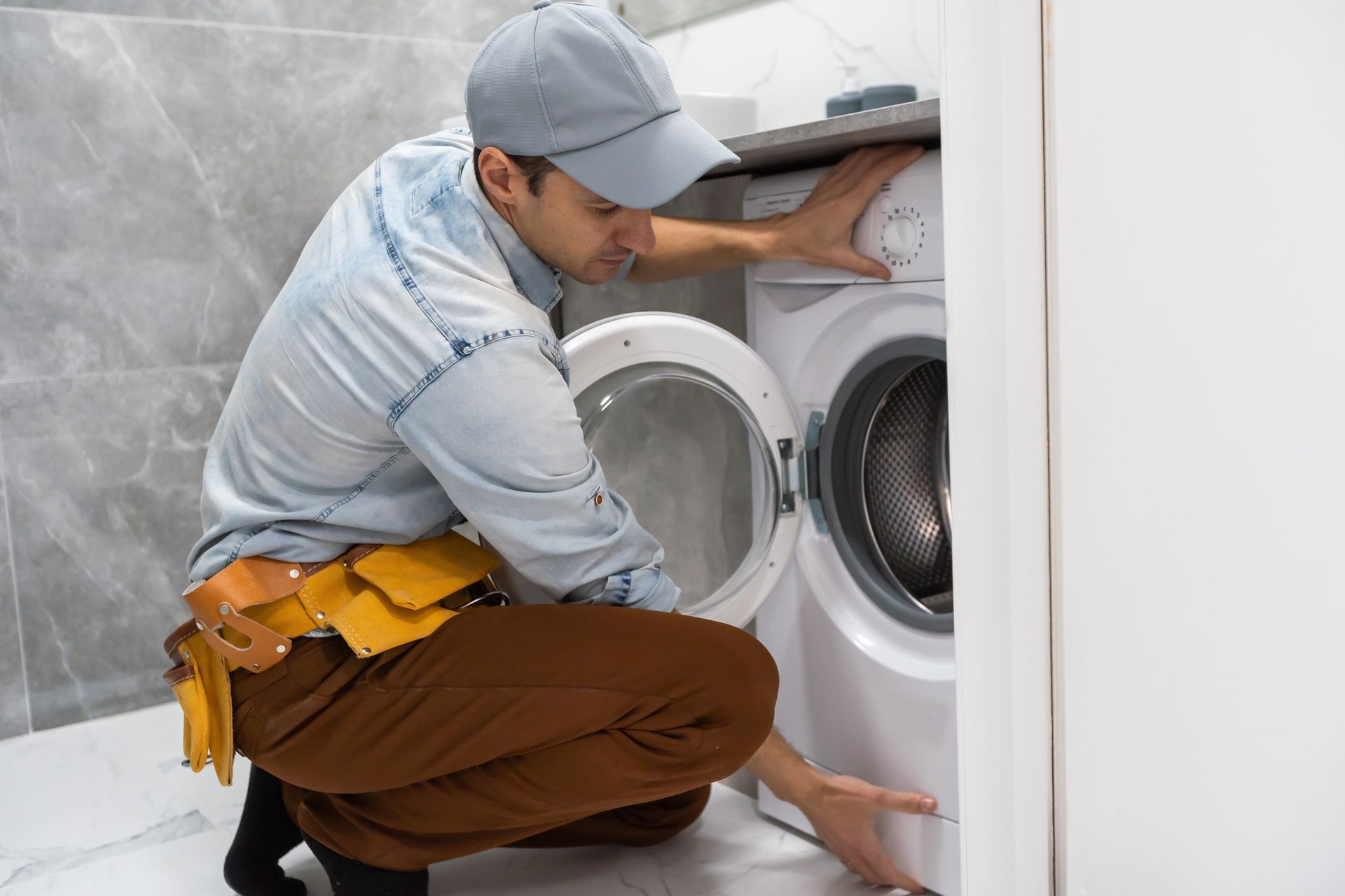 A man is fixing a washing machine in a bathroom.