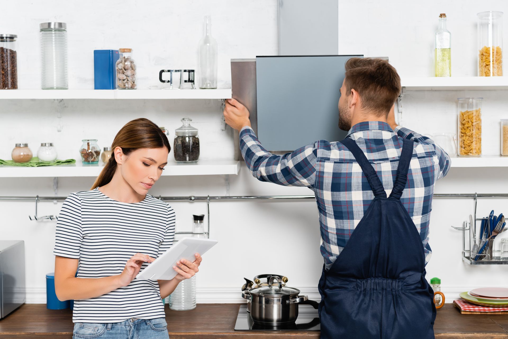 A man and a woman are standing in a kitchen looking at a tablet.