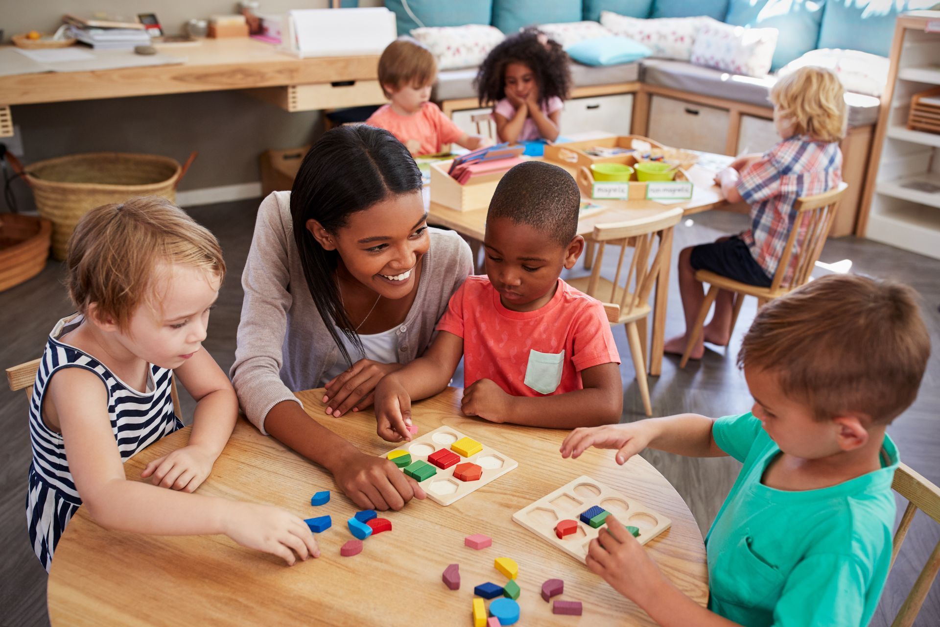 Children and a teacher gathered at a table working with colorful shape and puzzle activities. Children and a teacher gathered at a table working with colorful shape and puzzle activities.