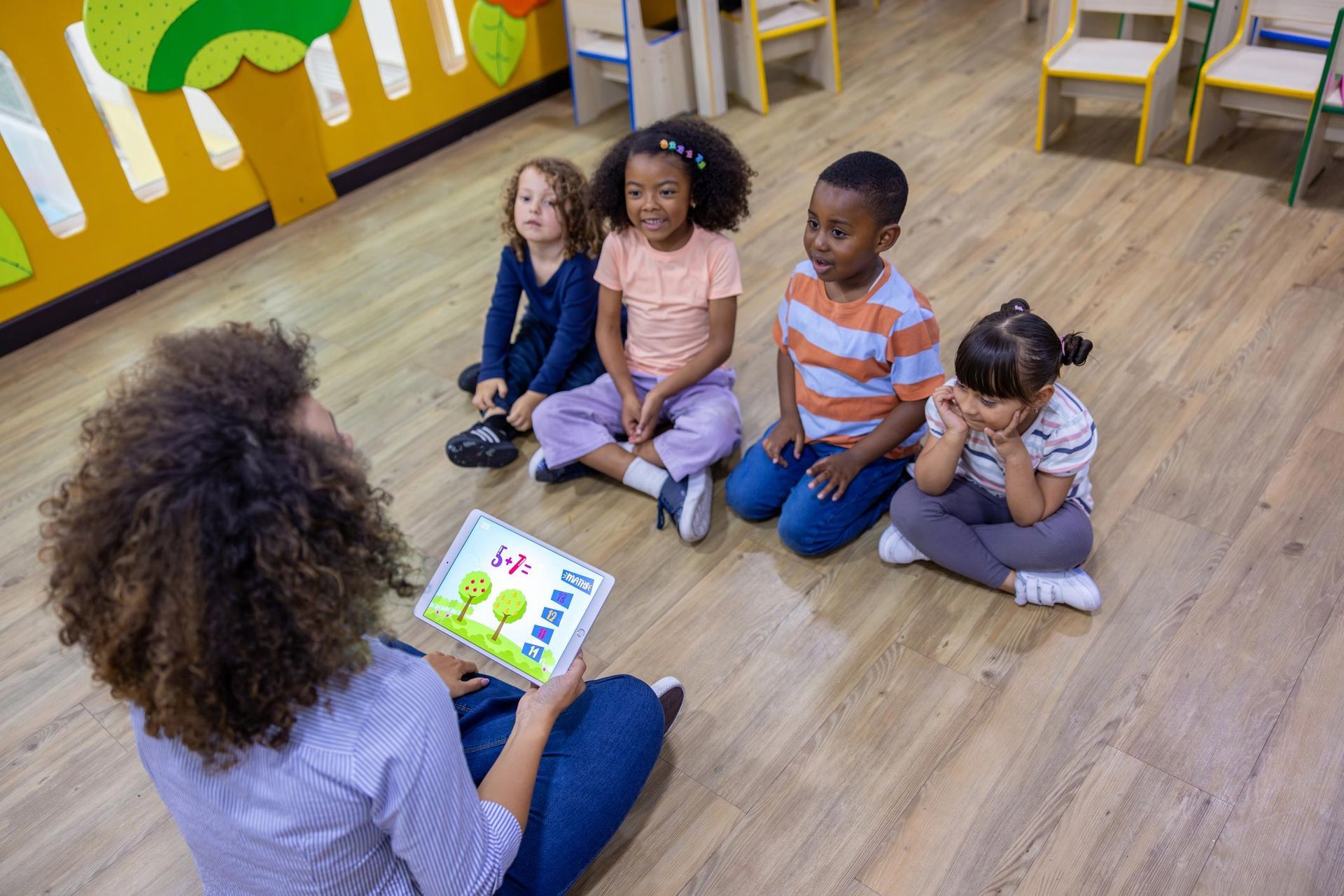 Preschool teacher using a digital tablet in math class with a group of children.