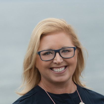 A woman wearing glasses and a necklace is smiling for the camera