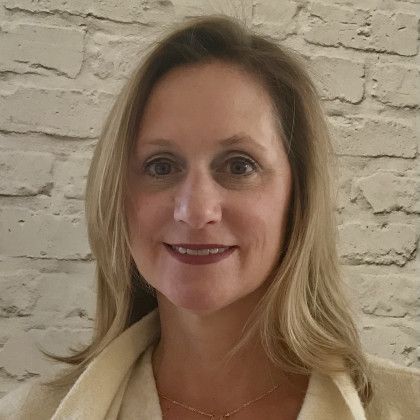 A woman is smiling in front of a white brick wall.