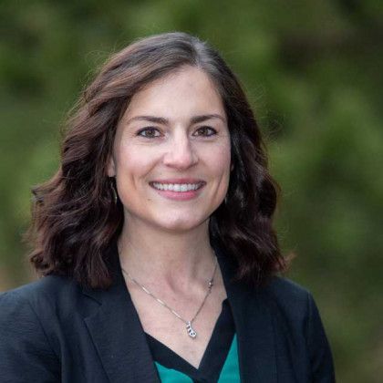 A woman wearing a black jacket and a green shirt is smiling for the camera.