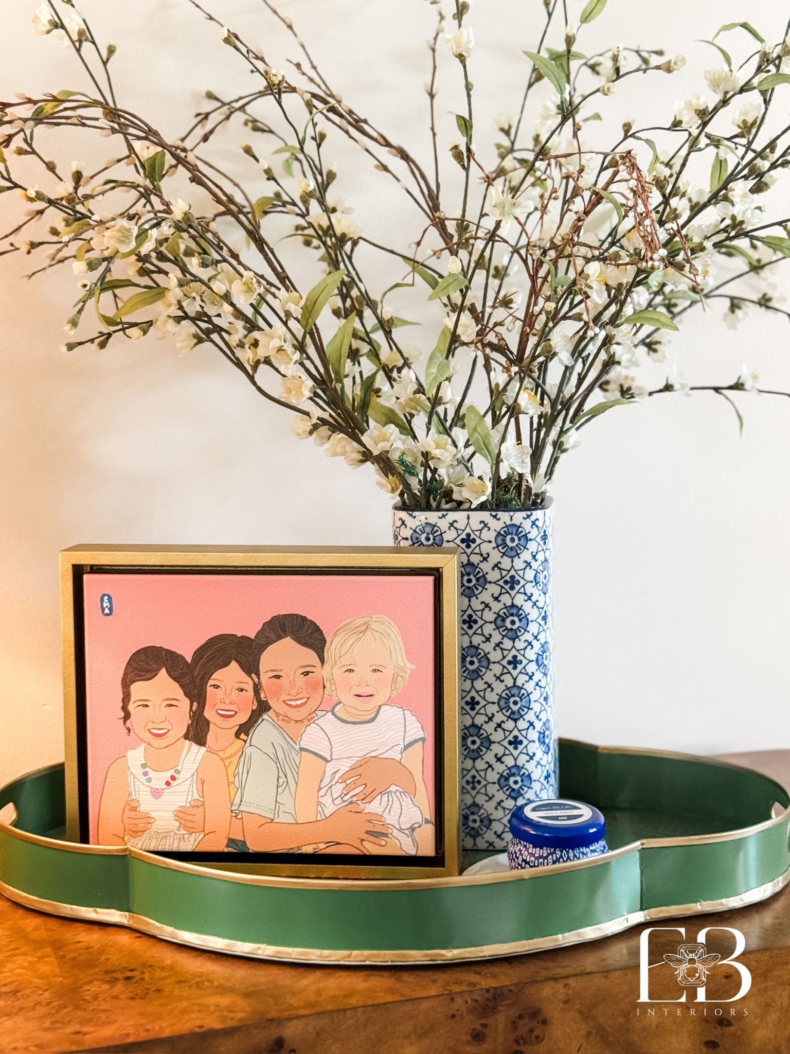 Family portrait in gold frame, vase of white flowers, blue and white vase on green tray.