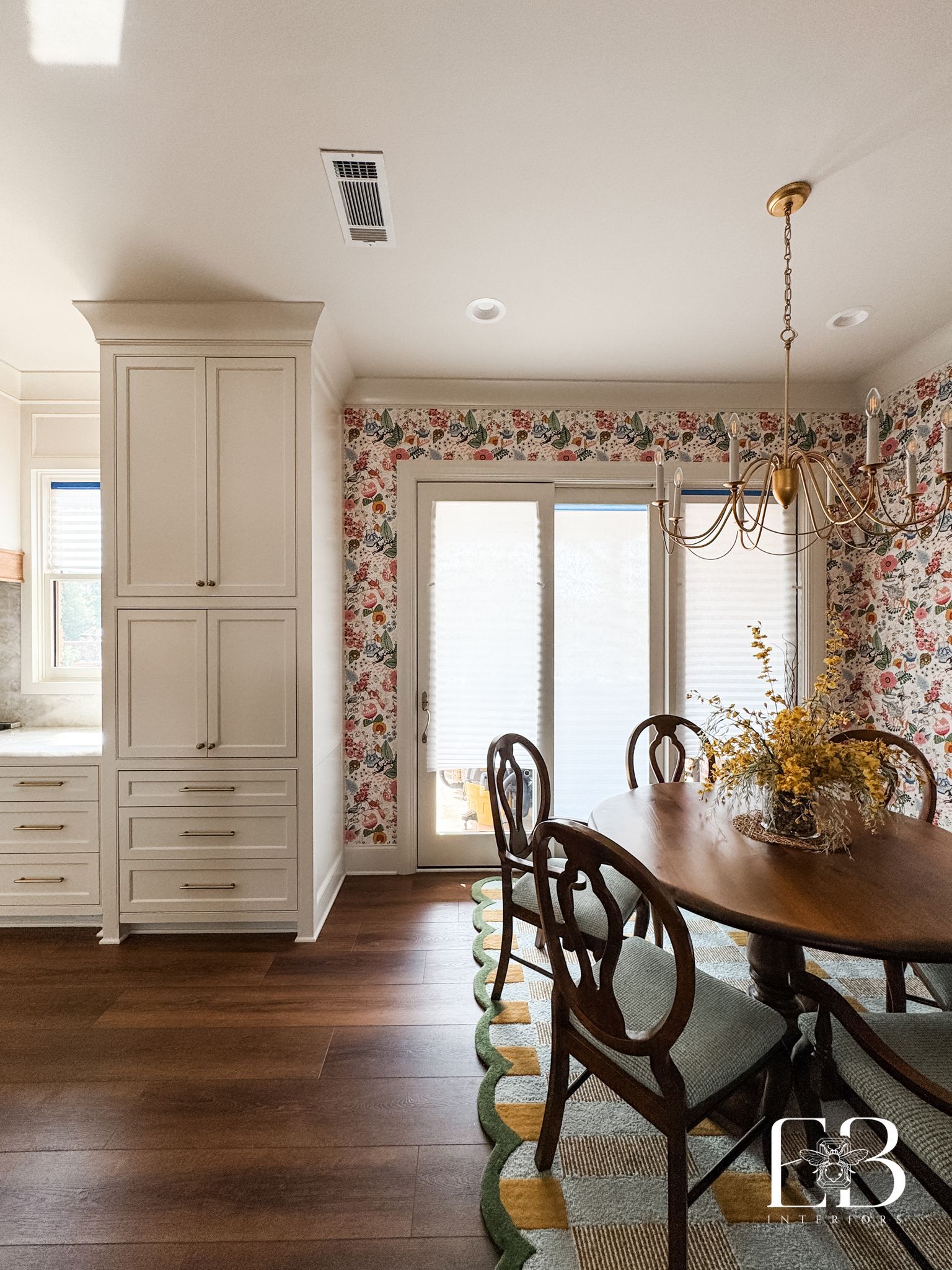 Dining room with floral wallpaper, wooden table, and chairs, white cabinetry, and a door to the outside.