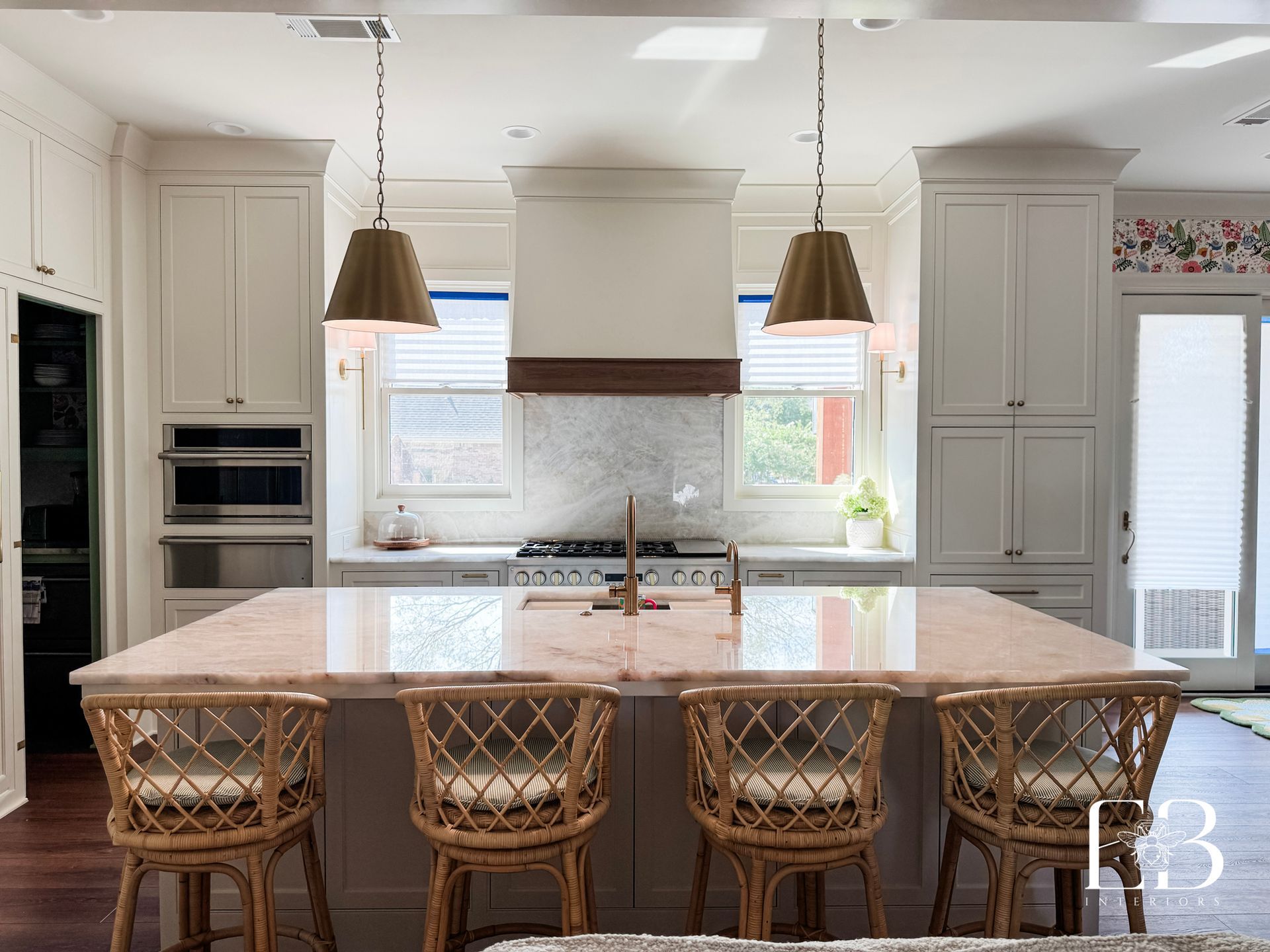 Kitchen with white cabinets, island with seating, copper light fixtures, and marble backsplash.