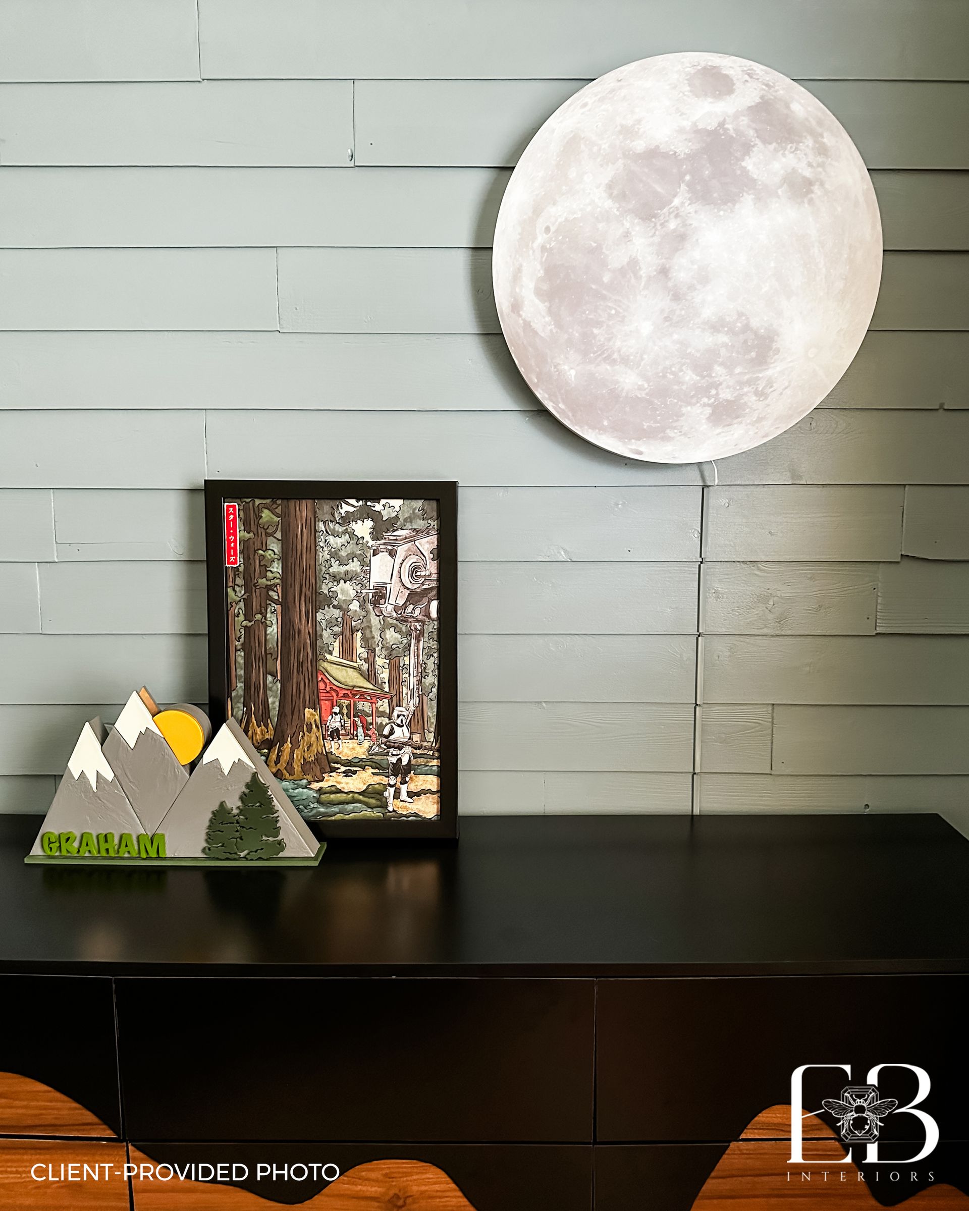 Black dresser with landscape art, moon light, and mountain decor on a gray wall.