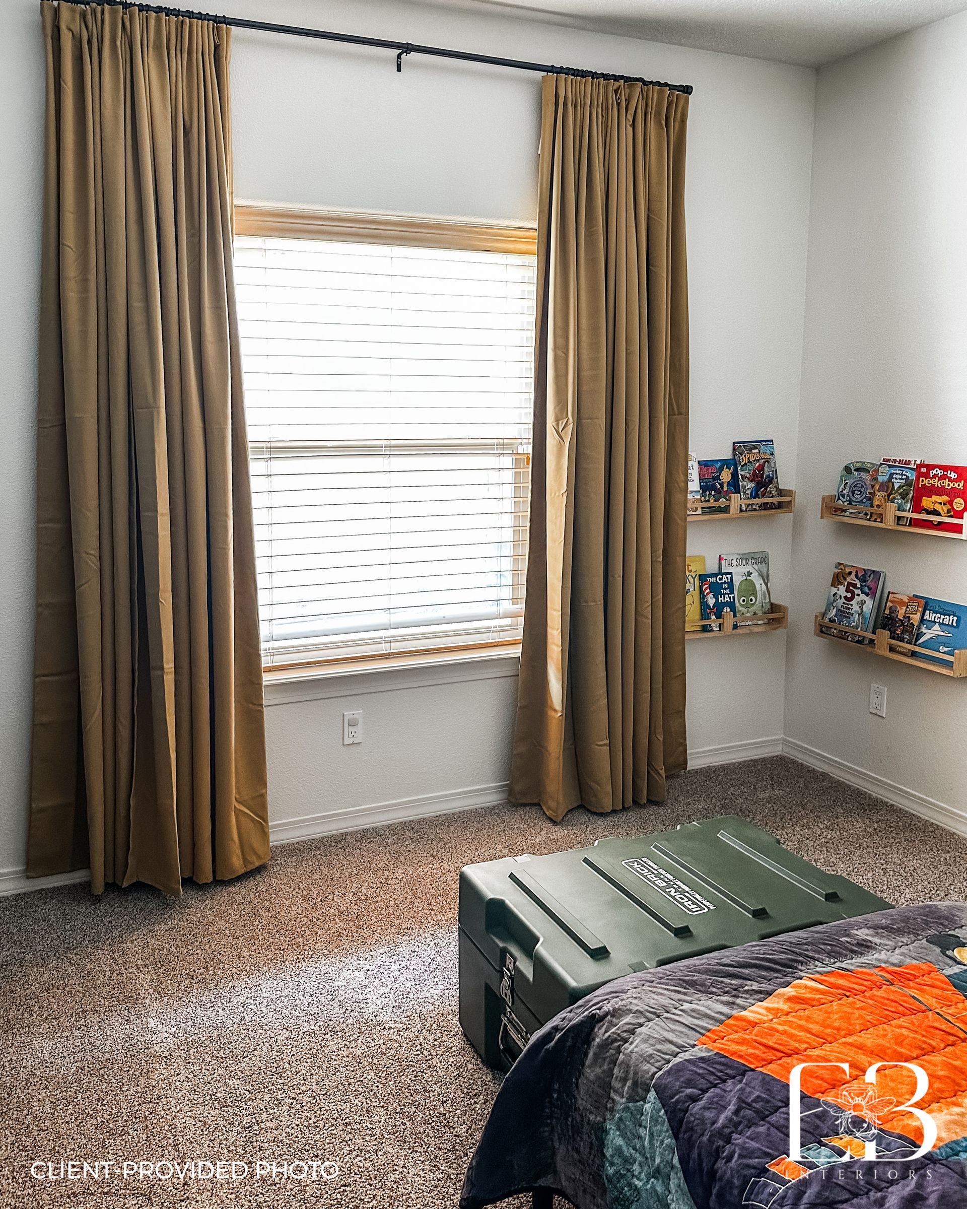 Bedroom with tan curtains, window, shelves of books, and a bed with a large green box at the foot.