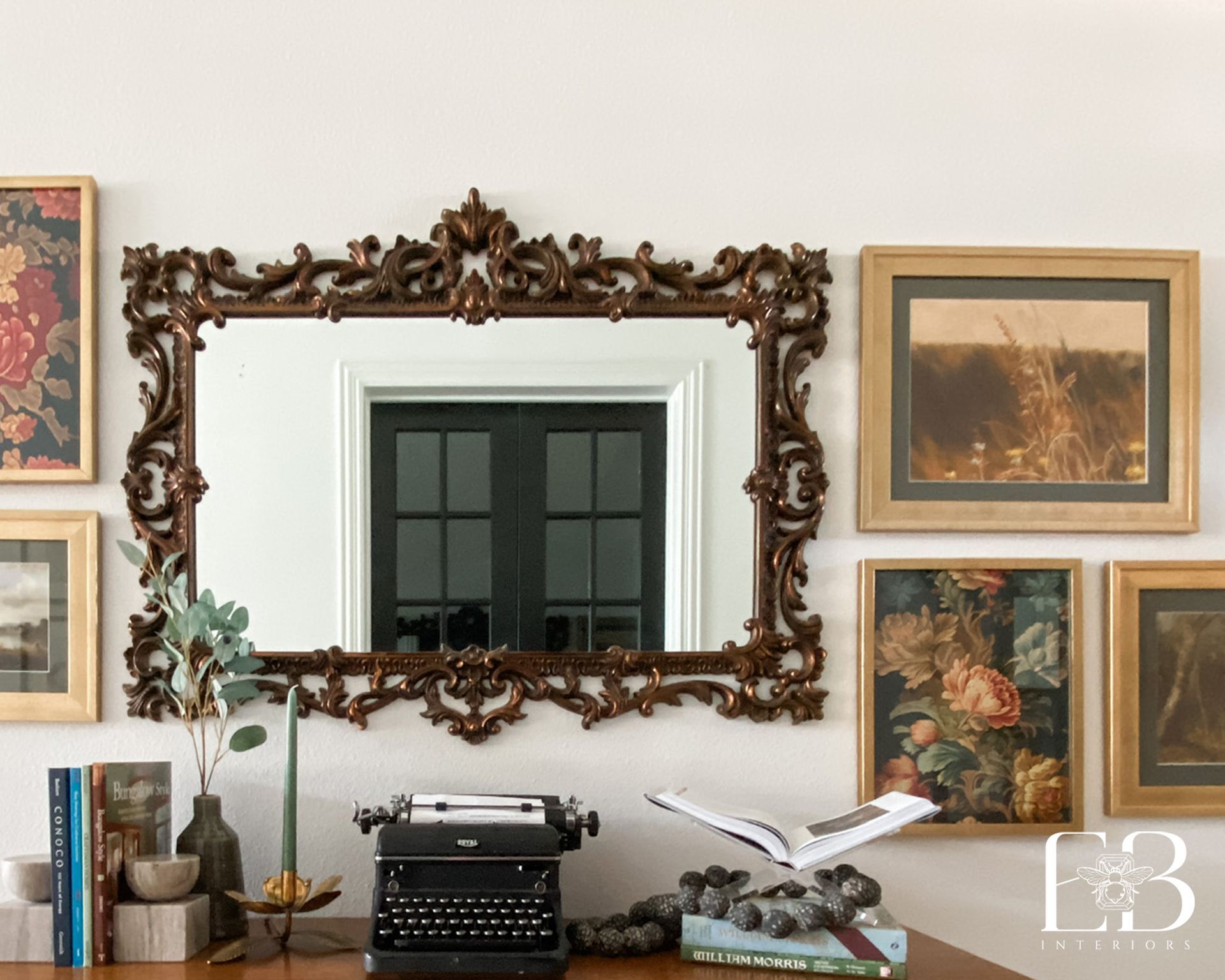 Ornate mirror above desk with framed art, typewriter, books, and candle.