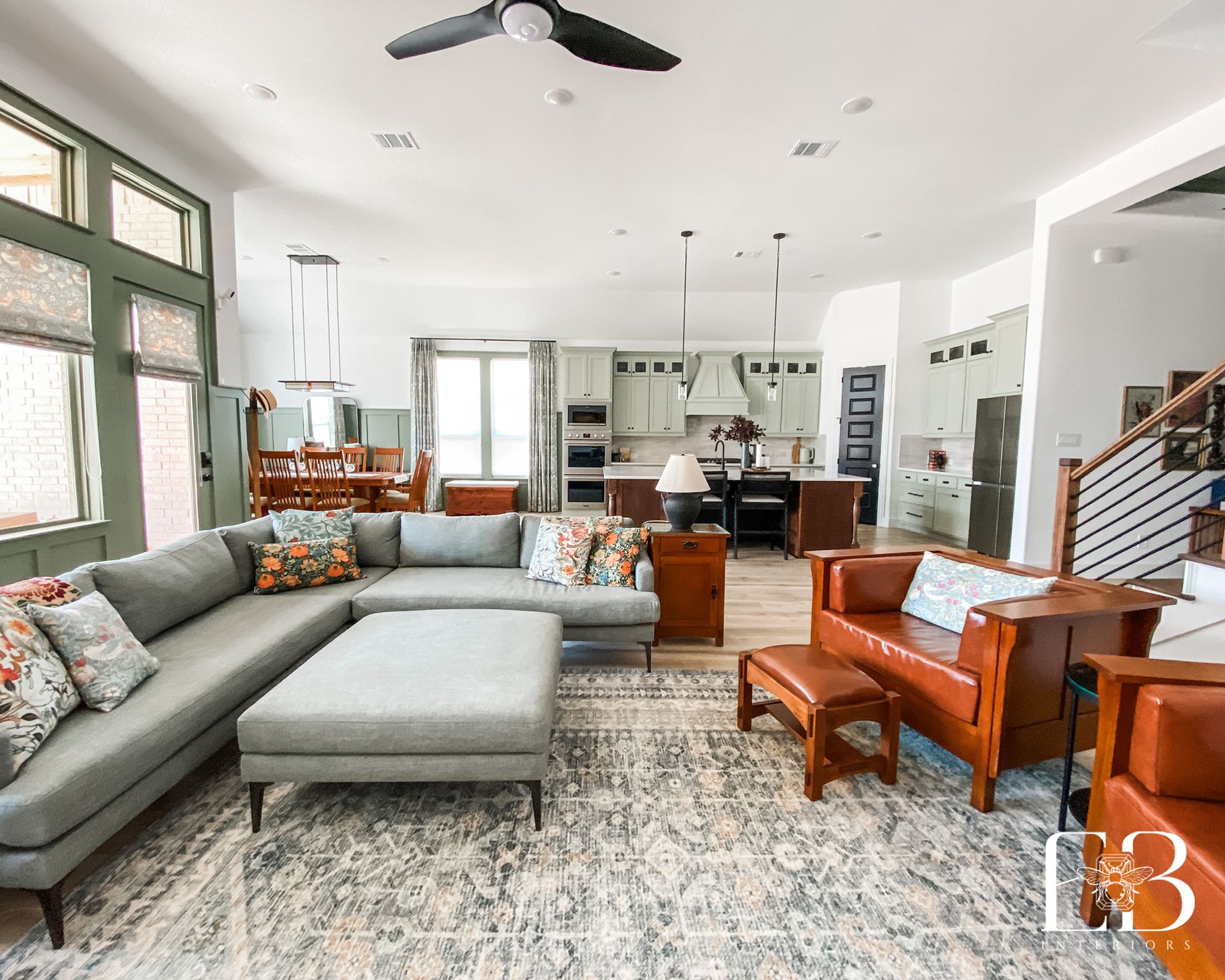 Living room with gray sectional sofa, wood furniture, and kitchen in the background.