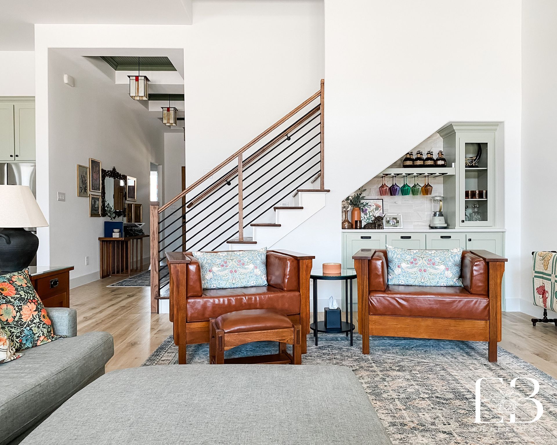 Living room with two brown leather armchairs, ottoman, staircase, and built-in bar.