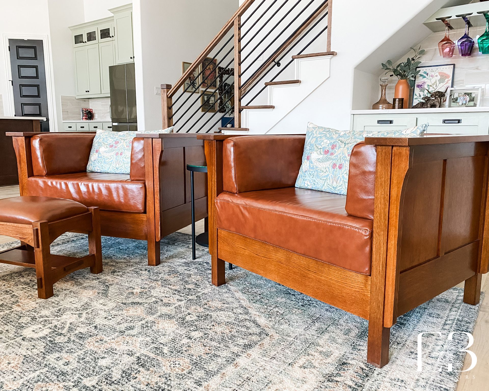 Living room with leather armchairs, ottoman, rug, stairs, and kitchen visible.