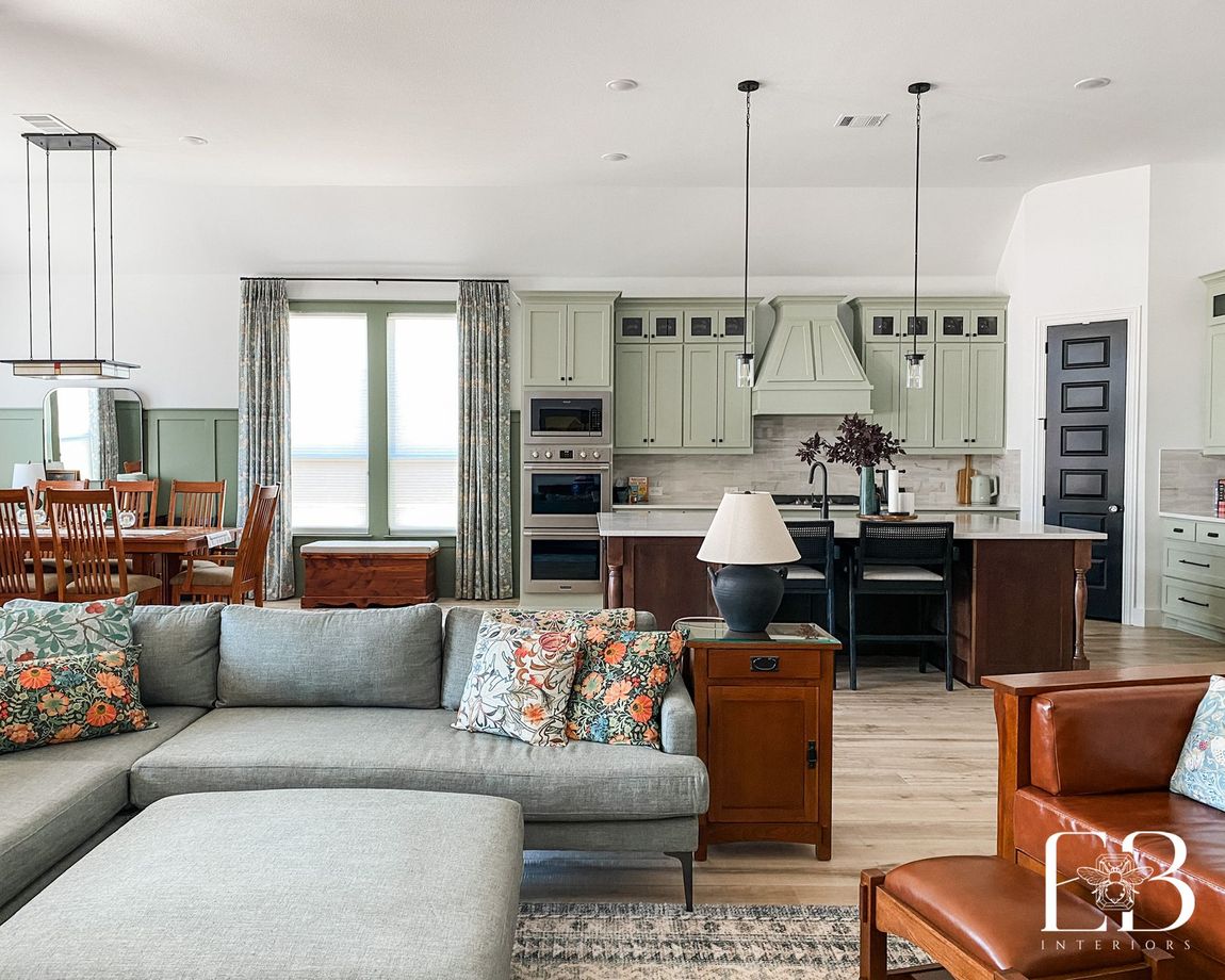 Open kitchen and living room with sage cabinetry, floral draperies, and mission-style furniture by Emerald Bee Interiors.