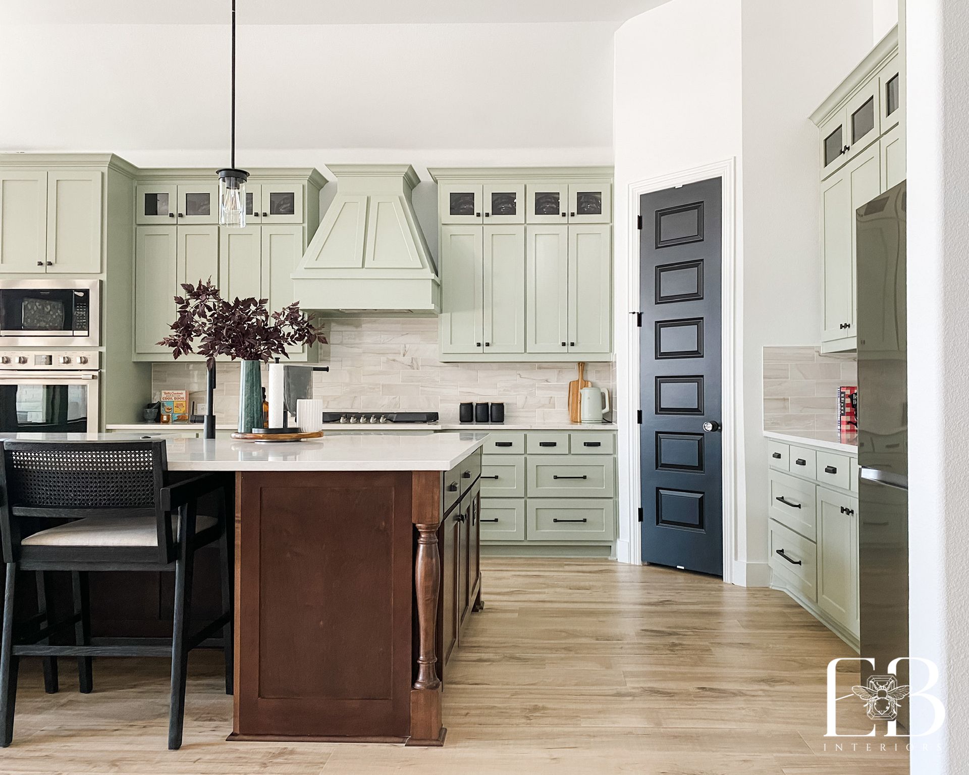 Kitchen with pale green cabinets, brown island, and black door.