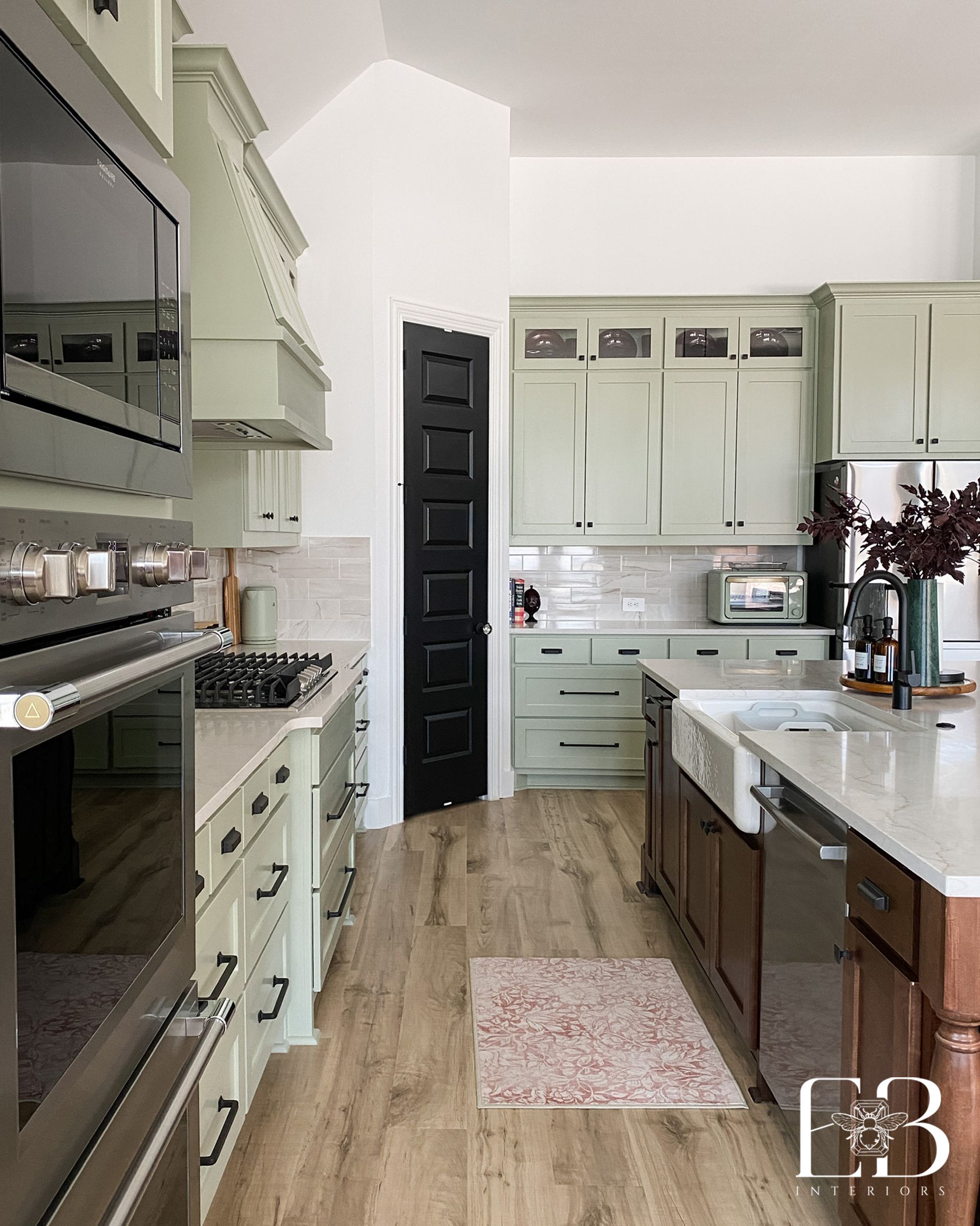 Green kitchen with black door, white countertops, and wooden floors.