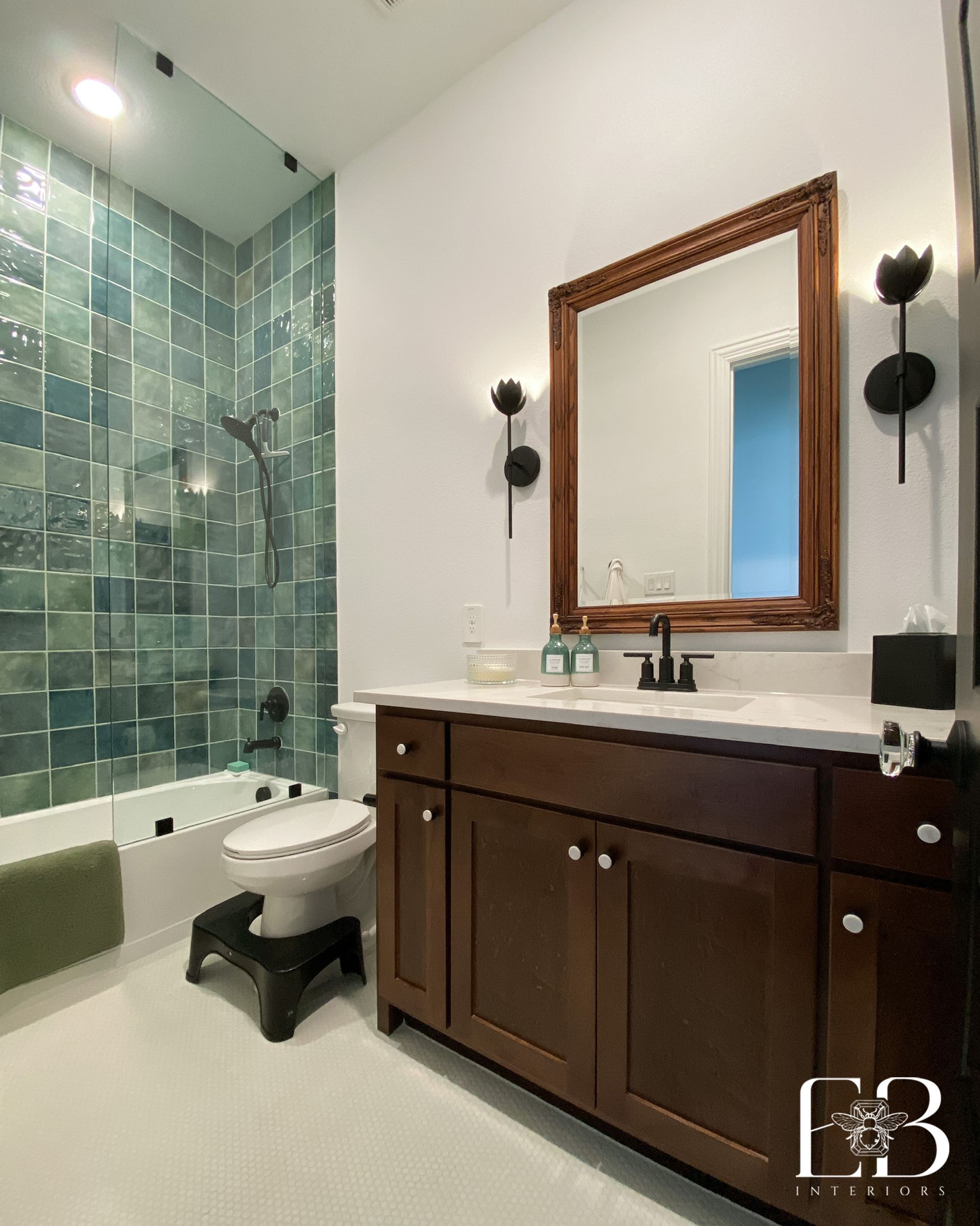 Bathroom with teal tile shower, dark wood vanity, white countertop, and brown framed mirror.
