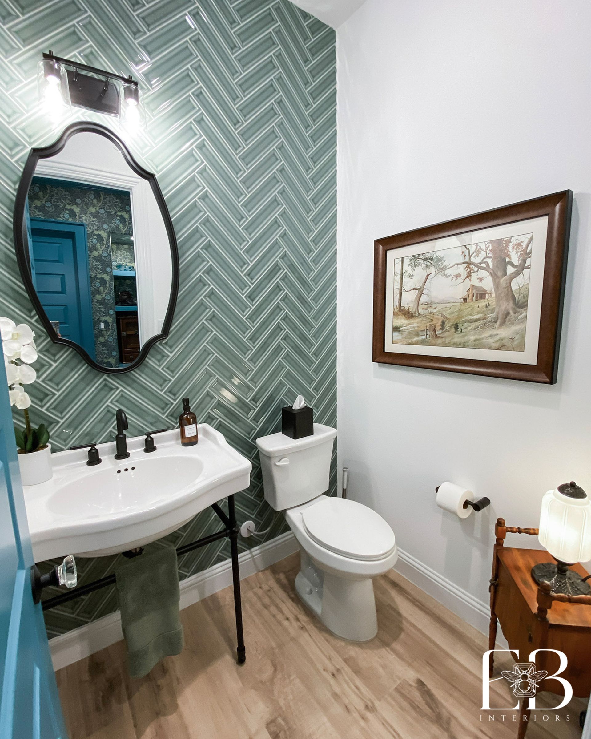 Small bathroom with patterned green wall, white fixtures, wood floors, and a framed picture.