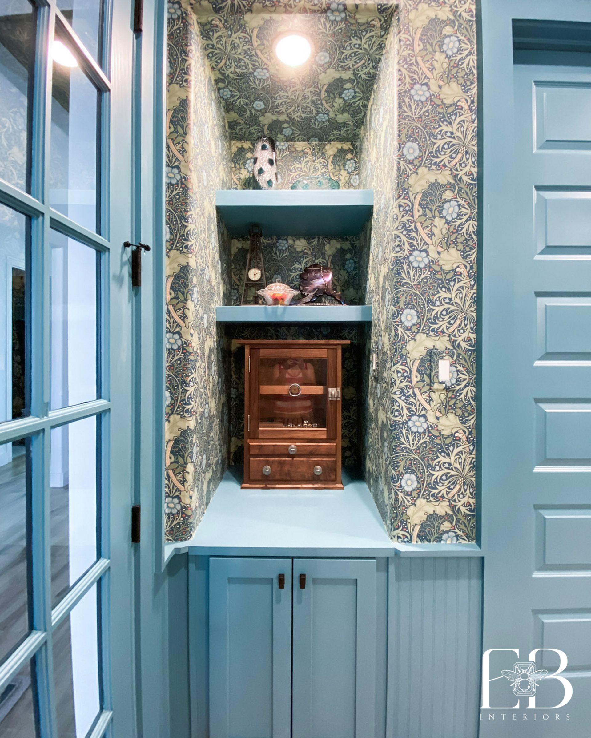 Built-in display niche with blue trim, patterned wallpaper, and a small wooden cabinet.