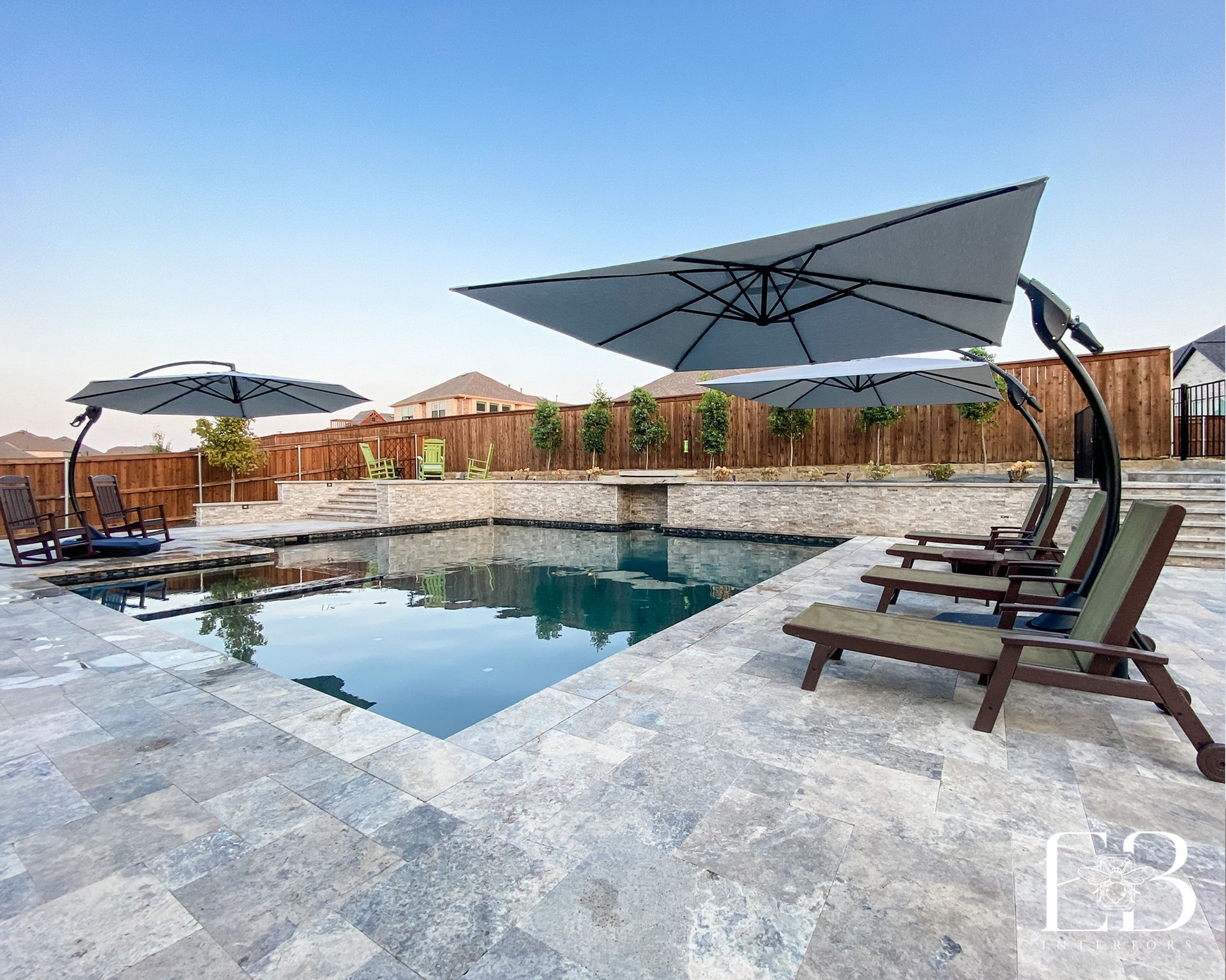 Swimming pool with lounge chairs, umbrellas, and stone patio under a blue sky.