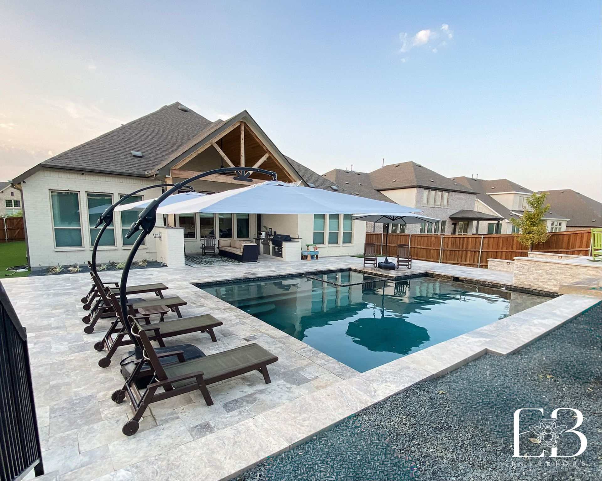 Backyard and pool at the Devotion Row home by Emerald Bee Interiors with modern lounge seating and travertine decking.