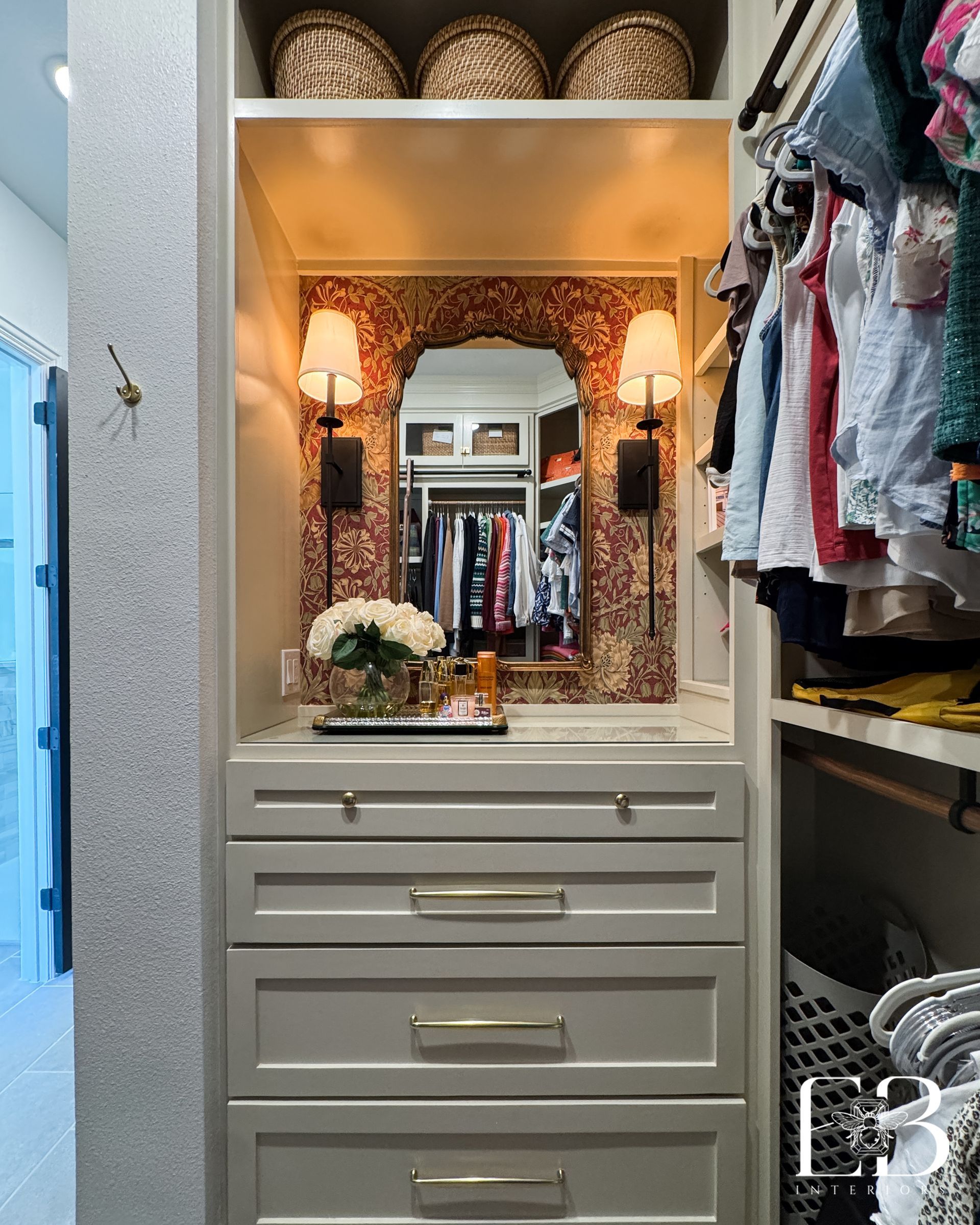 Custom vanity nook in walk-in closet with William Morris wallpaper, brass sconces, and florals by Emerald Bee Interiors.
