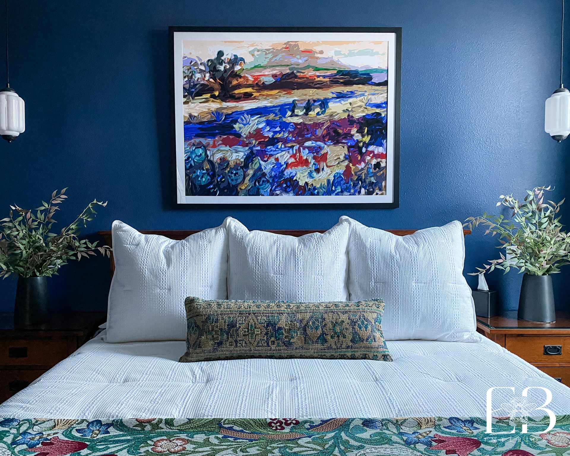 Bedroom with a navy blue textured wall, a bed with white pillows and a colorful painting.